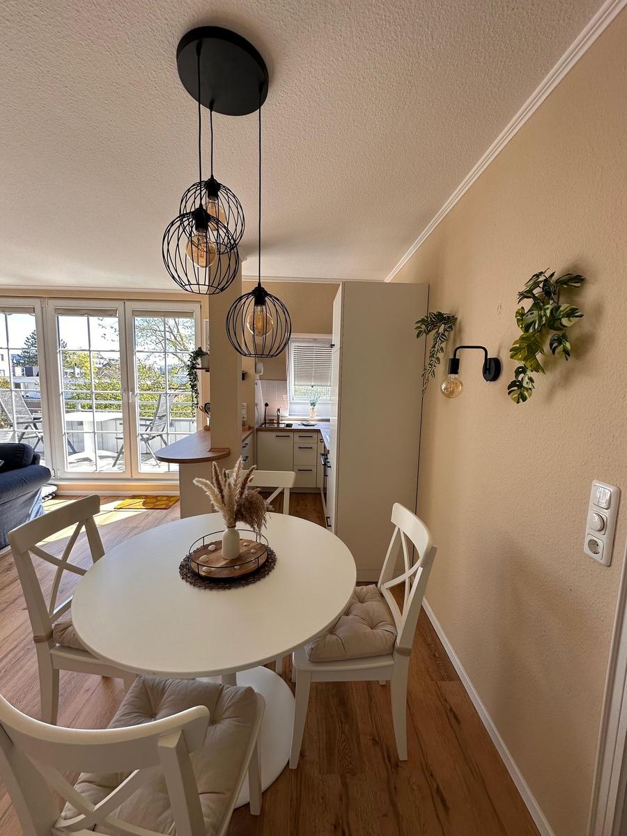 Rundes Esszimmer mit weißen Stühlen und hängenden Lampen. Küche und Terrasse im Hintergrund.