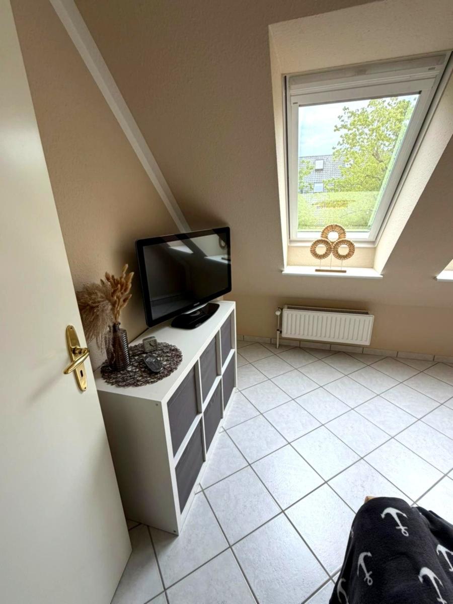 Dachgeschosszimmer mit TV, Fenster und Fliesenboden.