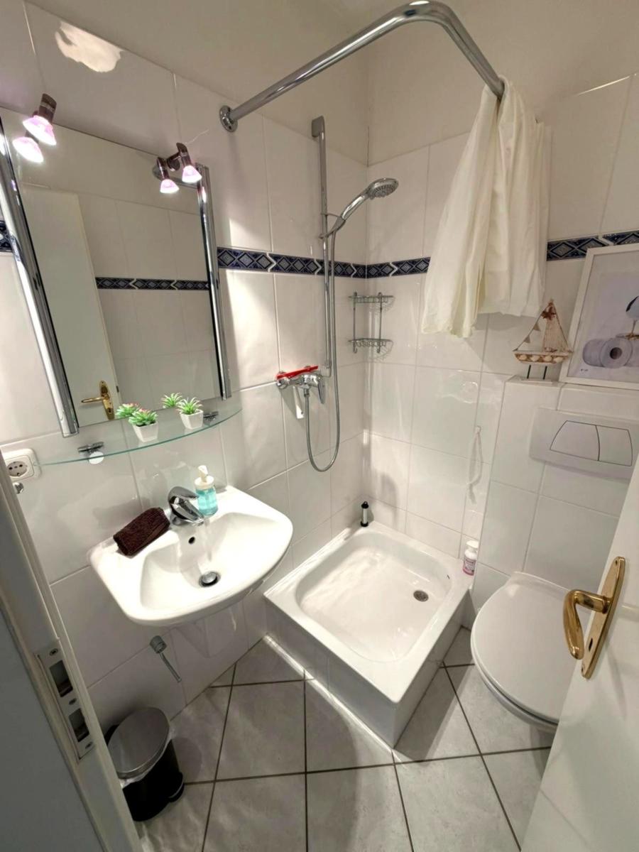 Badezimmer mit Dusche, Waschbecken und Toilette. Weiße Fliesen und Spiegelschrank.