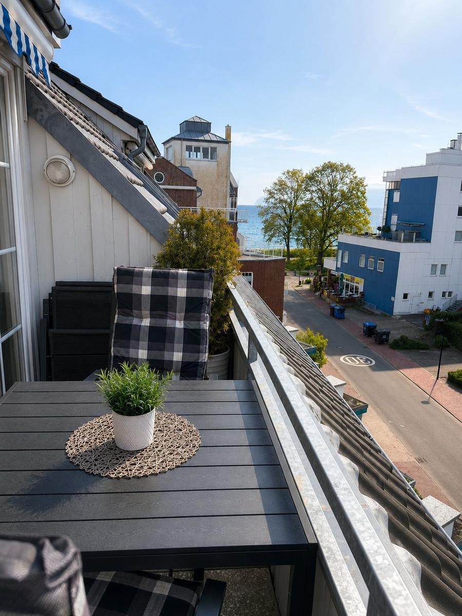 Terrasse mit Tisch, Stuhl und Pflanze. Blick auf Straße, Bäume und Meer.
