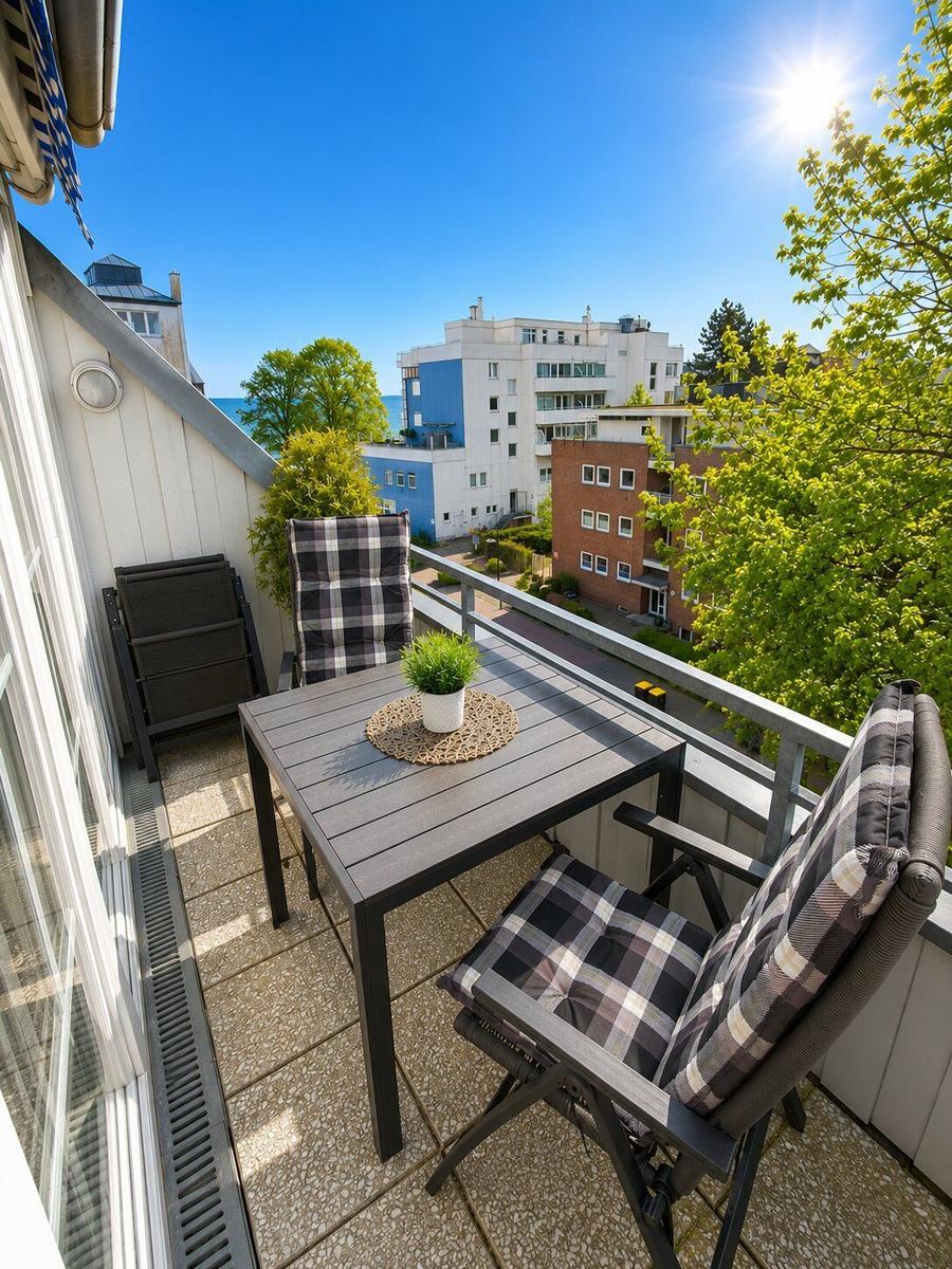 Terrasse mit Tisch, zwei Stühlen und Blick auf Gebäude und Bäume.