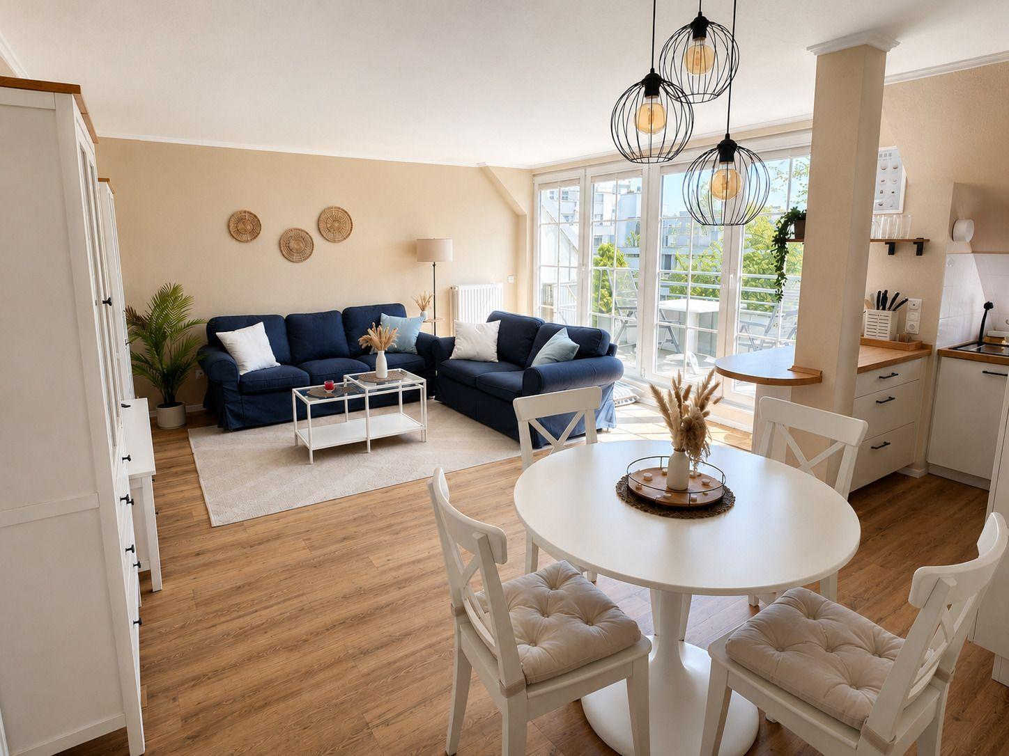 Wohnzimmer mit Essbereich, blauer Couch, weißen Stühlen und Holzboden.
