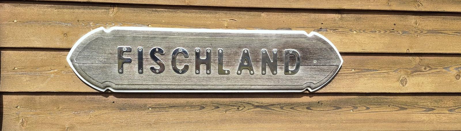 Holzschild mit der Aufschrift FISCHLAND an einer Holzwand