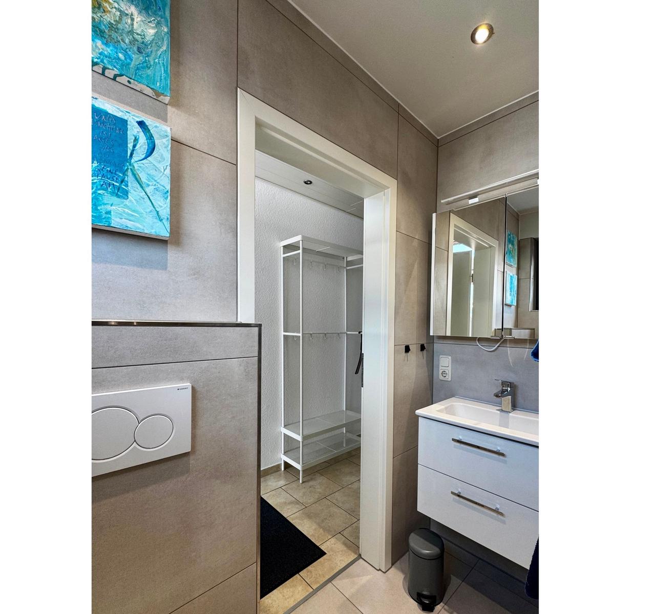 Badezimmer mit Waschbecken, Spiegel und Blick in die Garderobe.