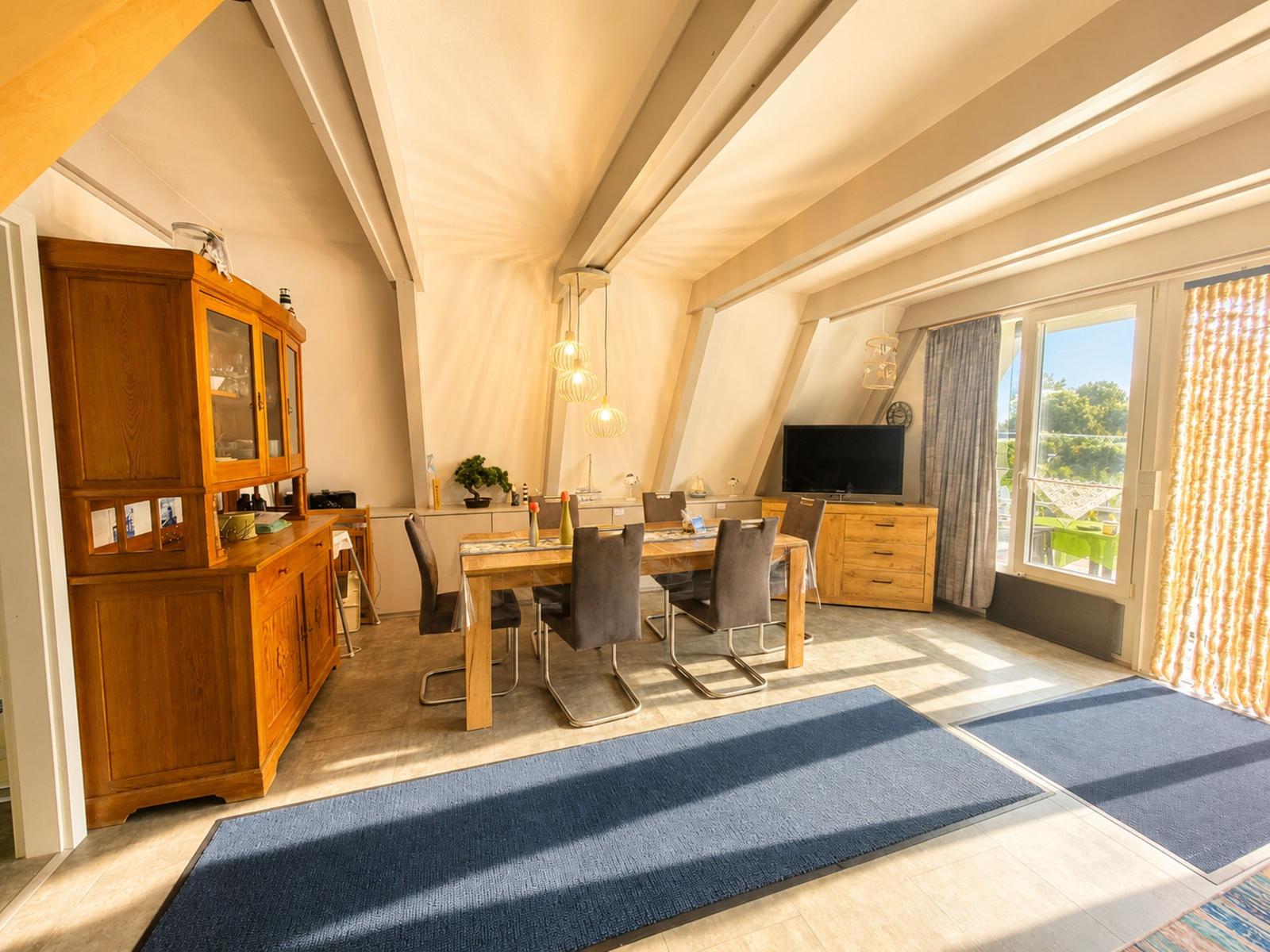 Esszimmer mit Holztisch, Stühlen und TV. Blick auf Balkon mit Garten.