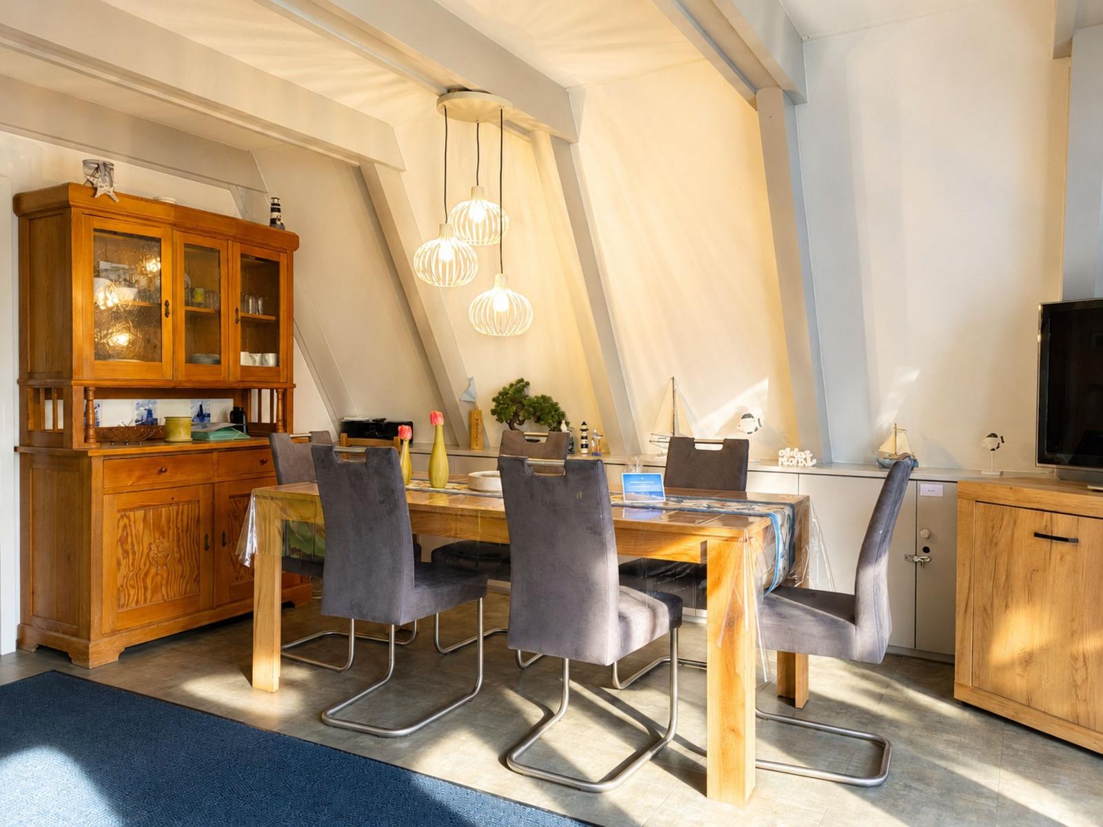 Essbereich mit Holztisch, grauen Stühlen und Holzschrank unter schrägen Dachbalken.