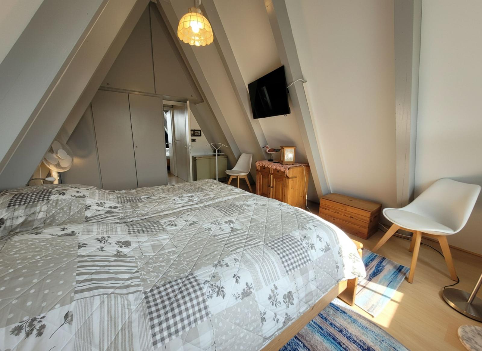 Schlafzimmer mit Dachschrägen, Bett, Fernseher und Stühlen.