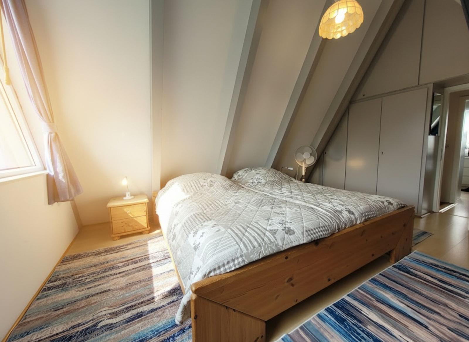 Schlafzimmer mit Holzbett, Kleiderschrank und Fenster. Decke mit Dachschrägen.