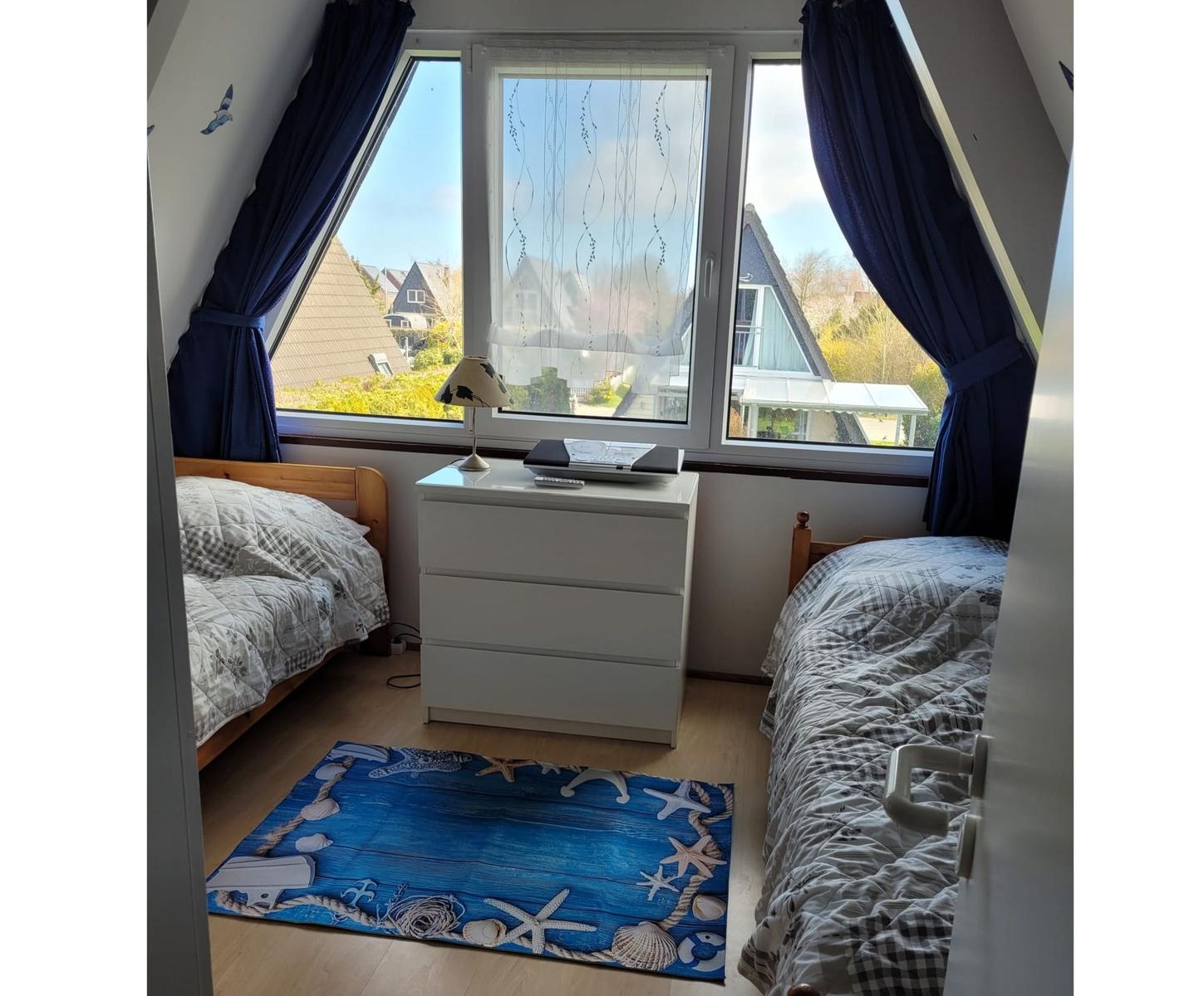 Zimmer mit zwei Betten, großem Fenster und blauem Teppich mit Meeresmotiven.