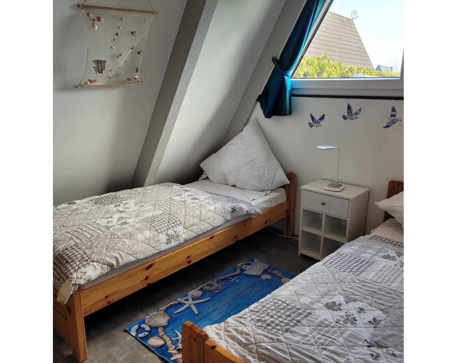 Zwei Betten mit Strandmotiv, Nachttisch und Fenster mit Blick.