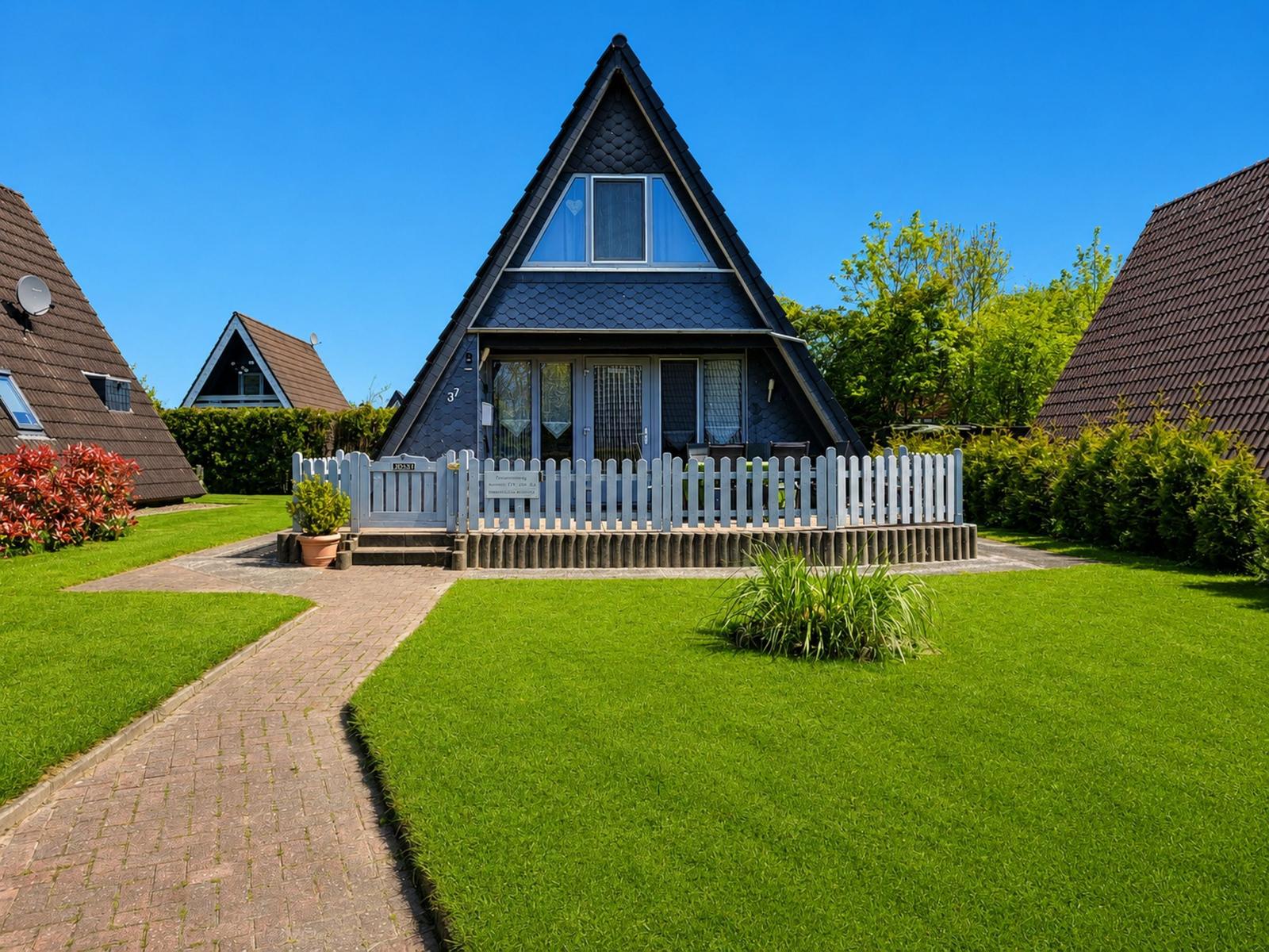 A-frame-Haus mit weißem Zaun und grünem Rasen vor einem klaren blauen Himmel.