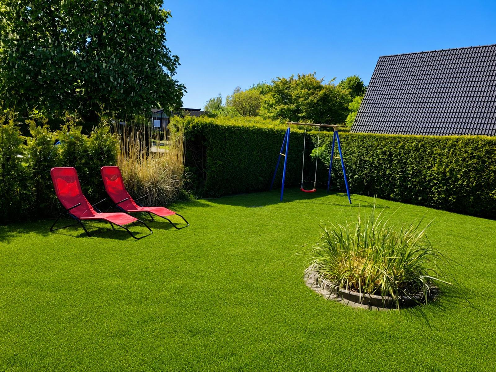 Roter Liegestuhl und Schaukel im grünen Garten mit Hecke und Haus.