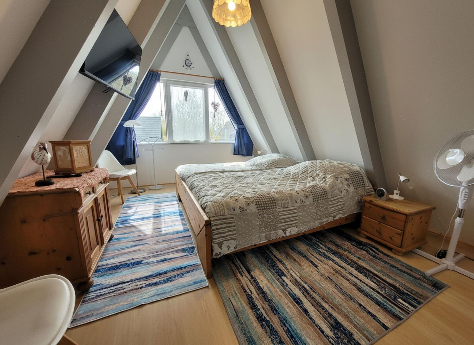 Schlafzimmer mit Dachschrägen, Bett, Schrank, Fenster und Ventilator.