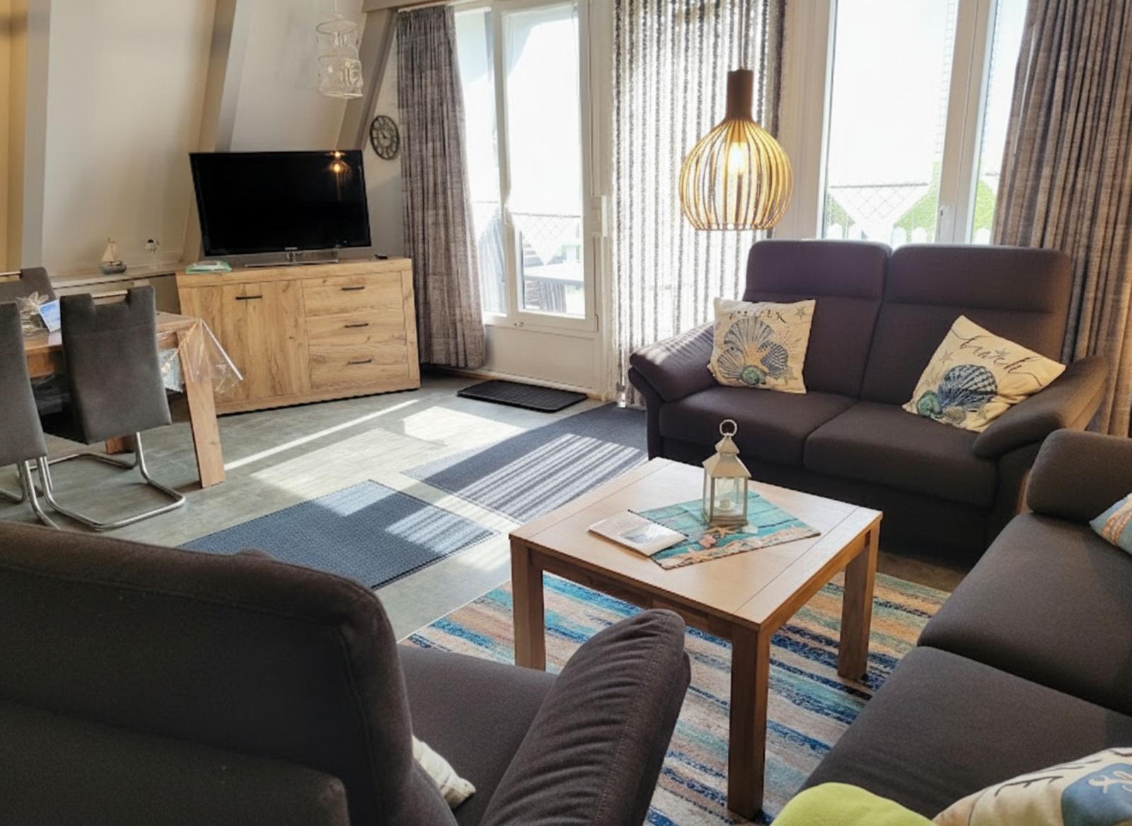 Wohnzimmer mit Sofa, Couchtisch und TV. Große Fenster mit Blick.