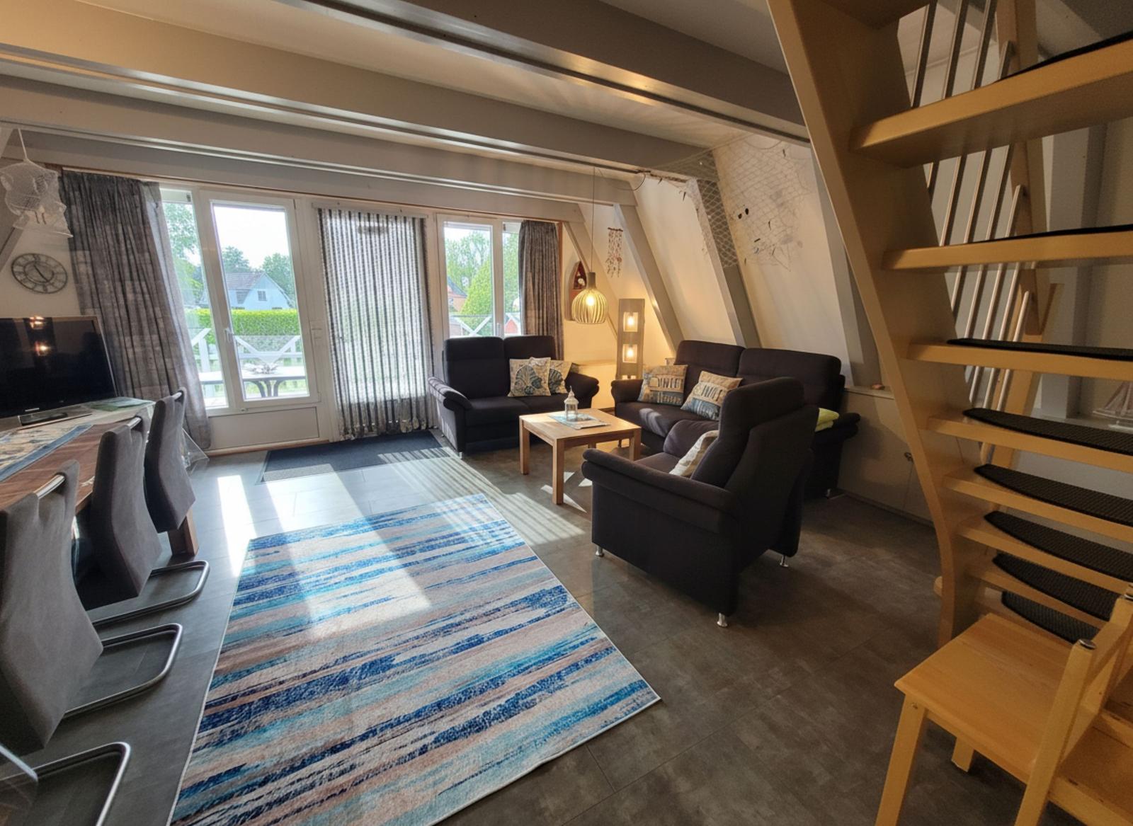 Wohn- und Essbereich mit Sofa, Tisch und Stühlen sowie Holztreppe.