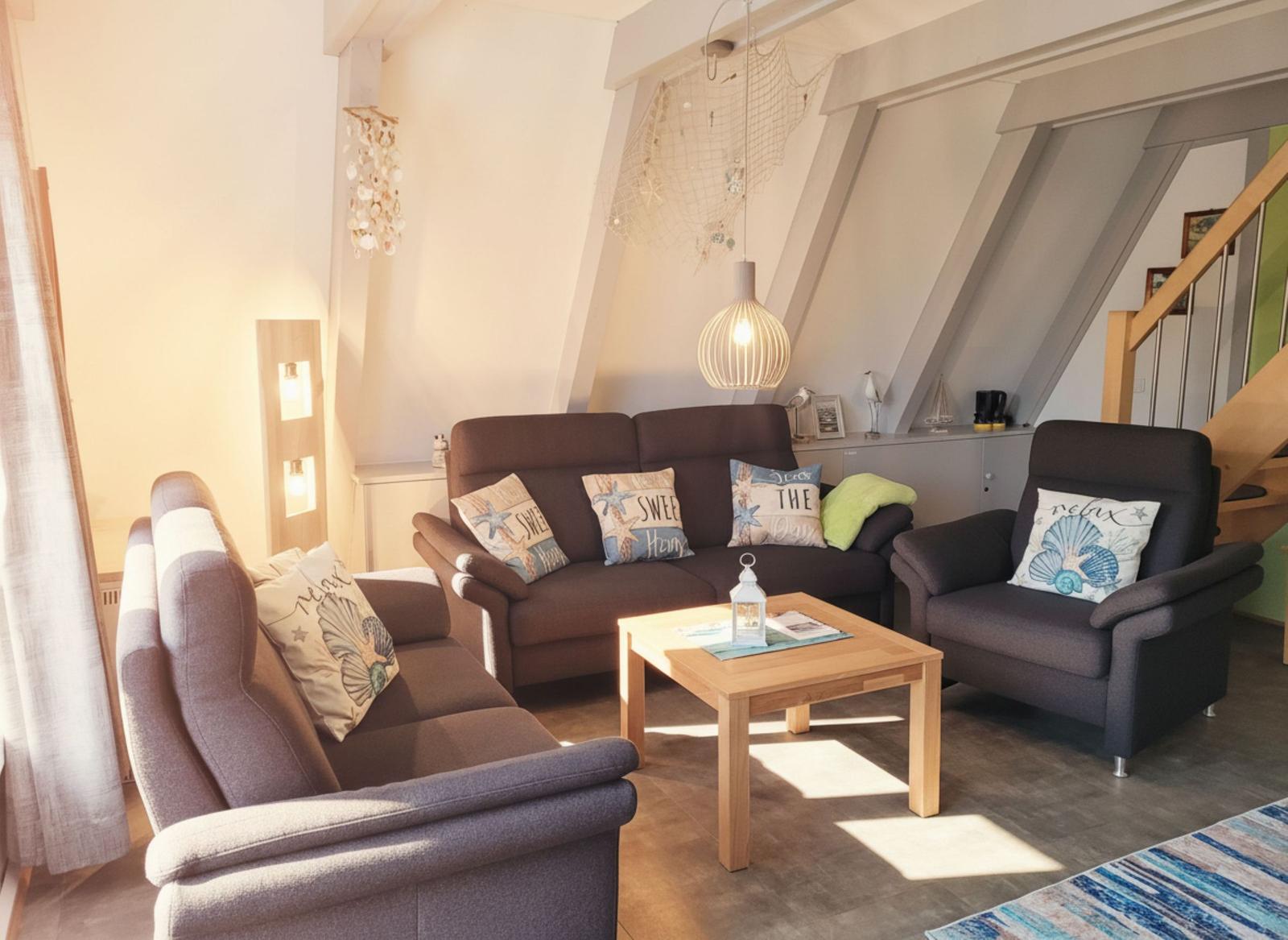 Wohnzimmer mit Sofa, Sessel und Holztisch unter schrägen Dachbalken.