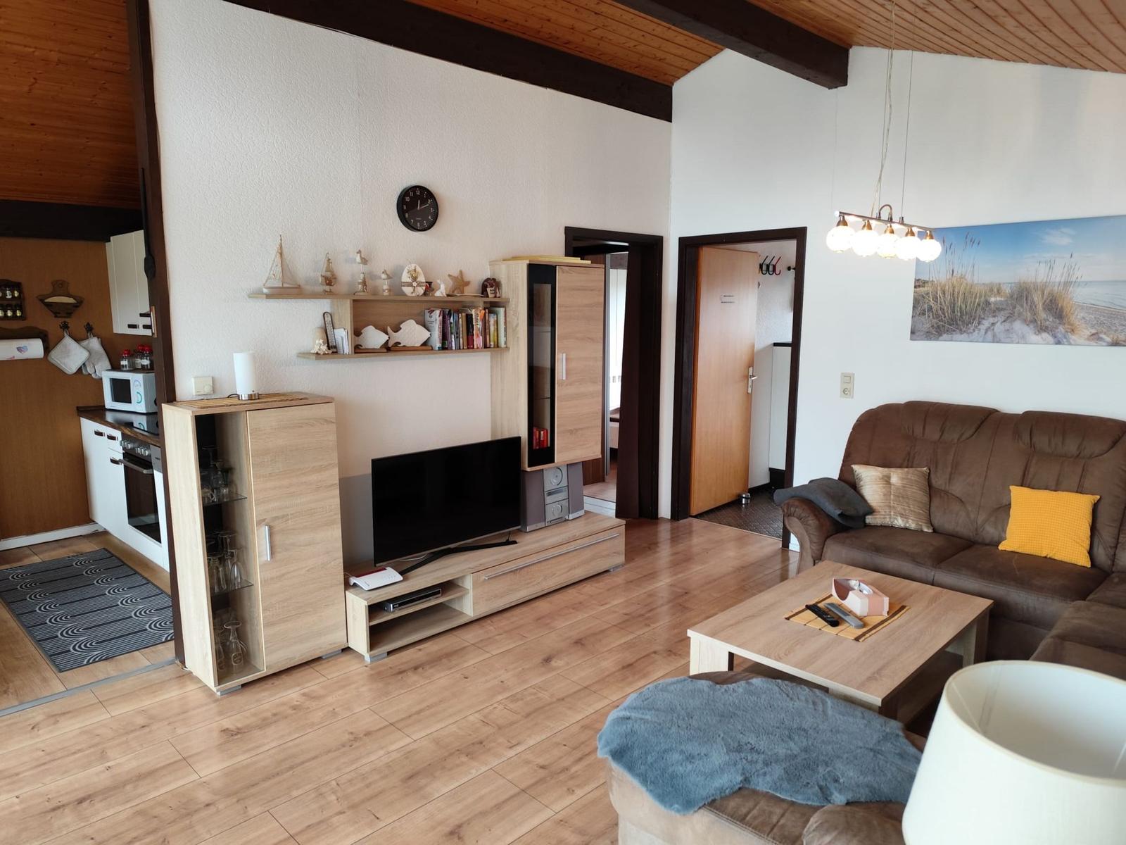Living room with sofa, TV, and kitchen area. Wooden floor and wall decoration.