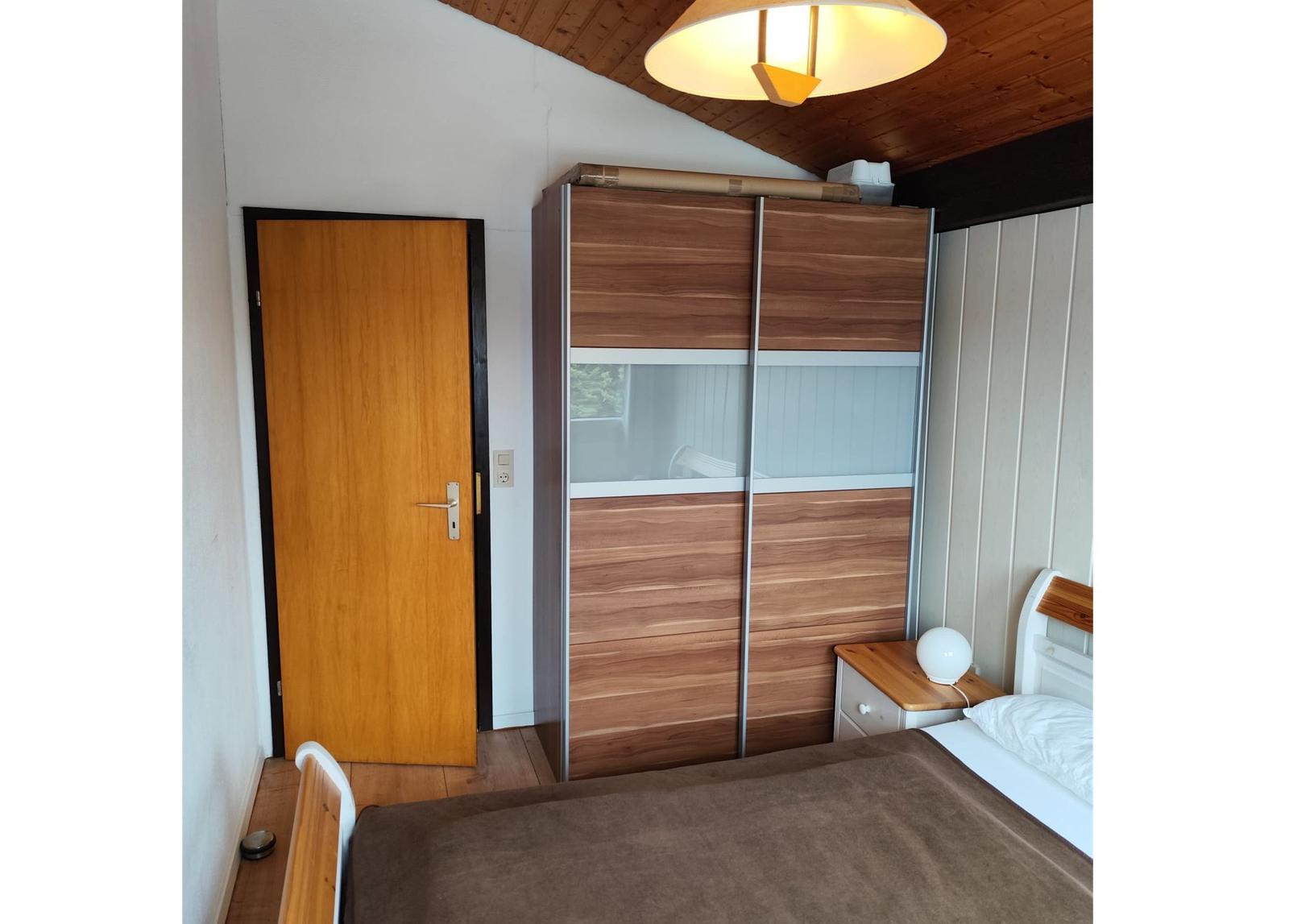 Bedroom with bed, wardrobe, and door. Wooden ceiling and nightstand with lamp.