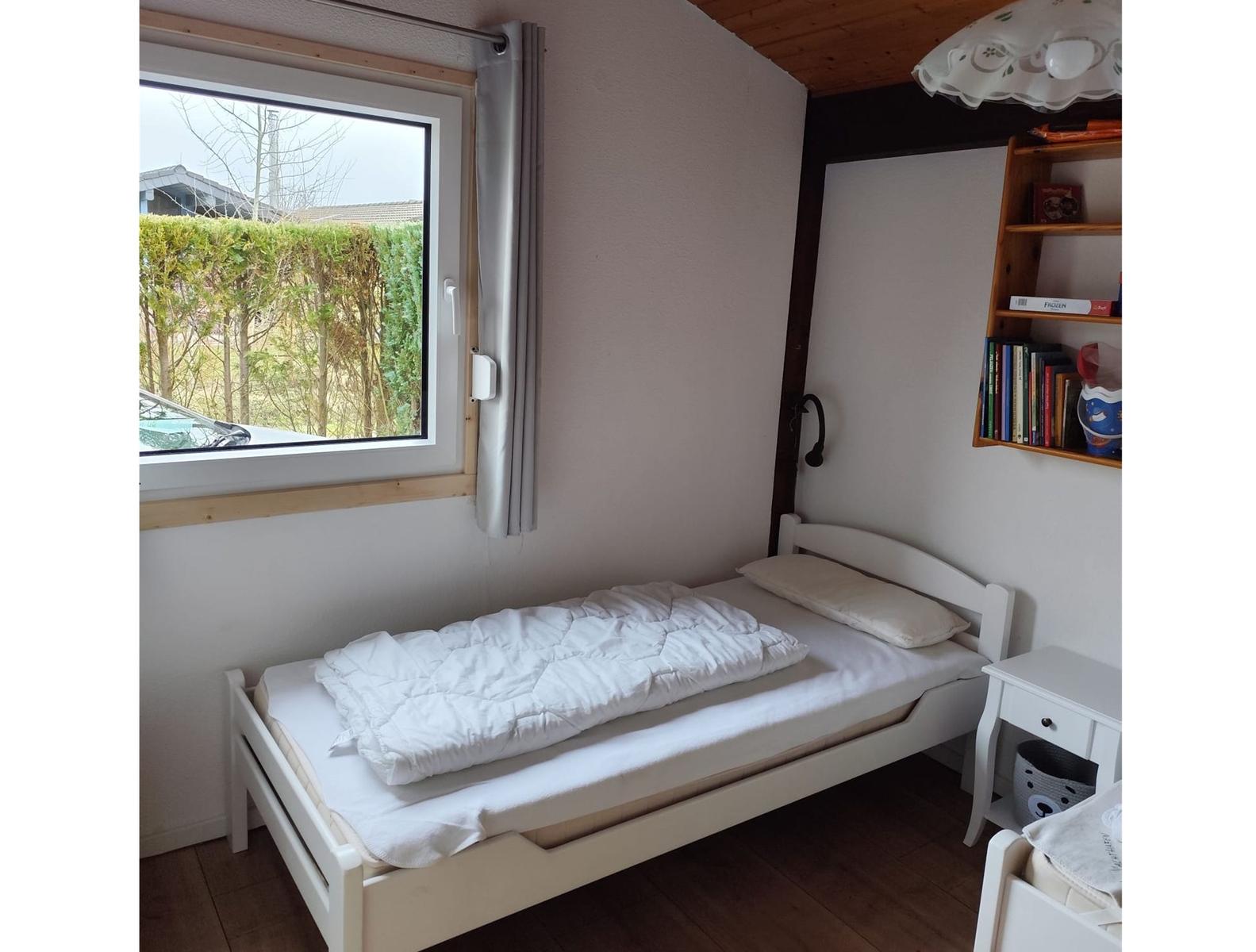 A bedroom with a white bed, window, and bookshelf.