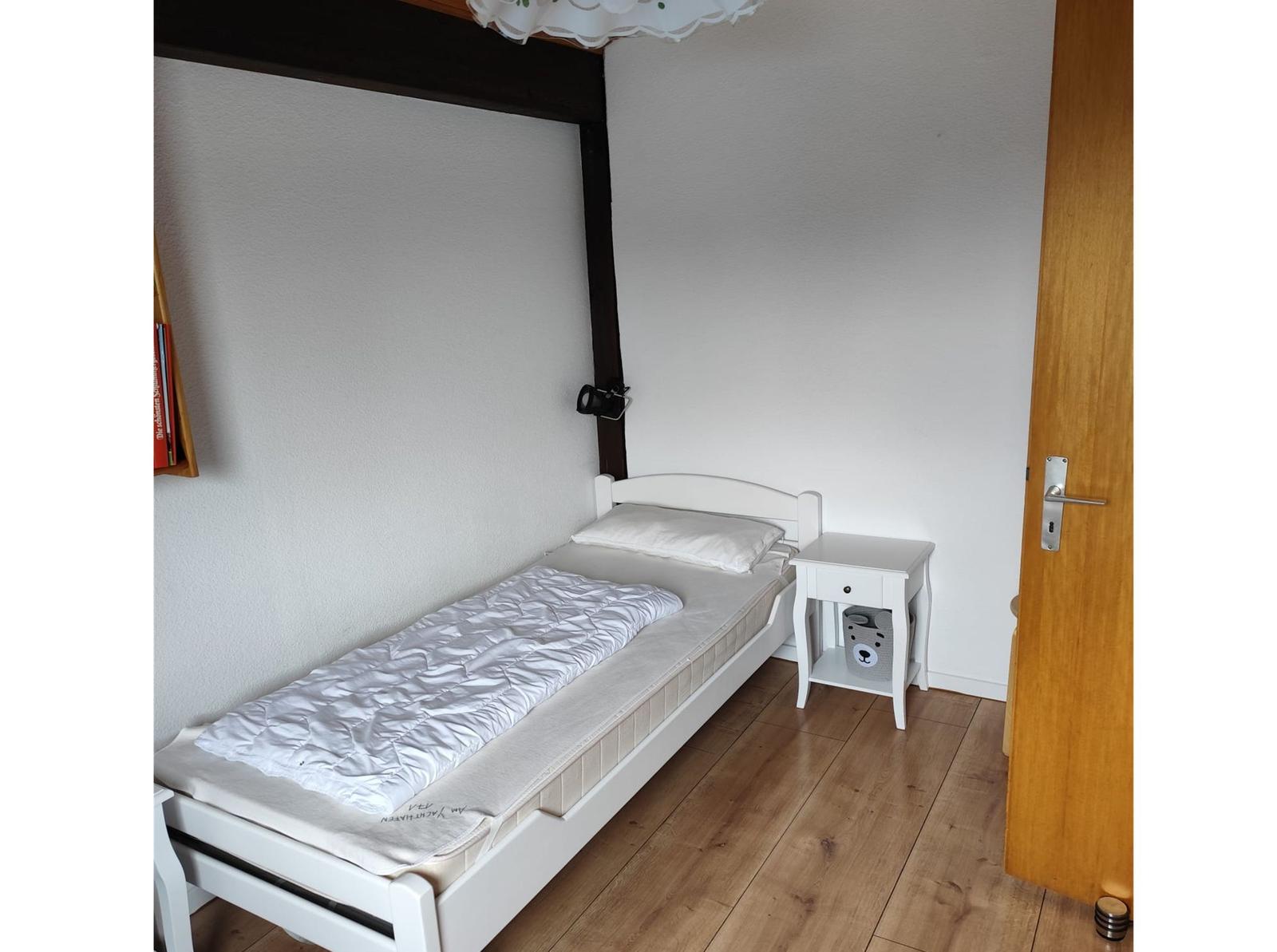 A bedroom with a white bed, nightstand, and wooden floor.