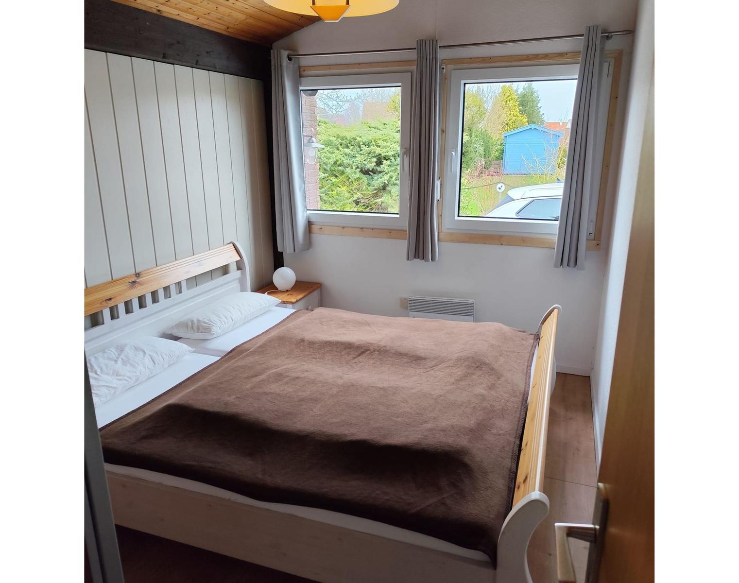 Bedroom with bed, windows, and wooden ceiling.