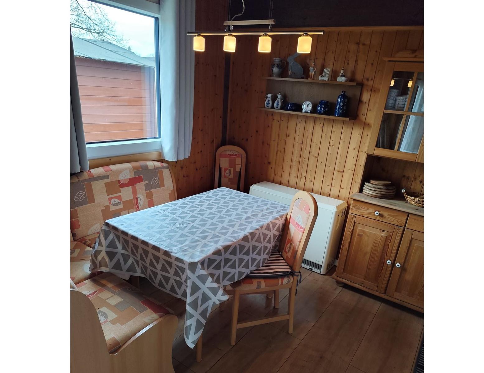 Dining room with wooden walls, table, chairs, and window. Tablecloth is on the table.