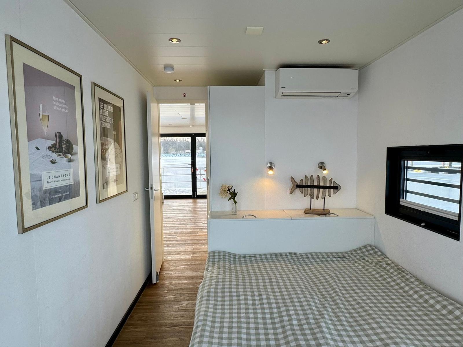 Schlafzimmer mit Bett, Wandbildern und Fenster. Durchgang zur Terrasse.