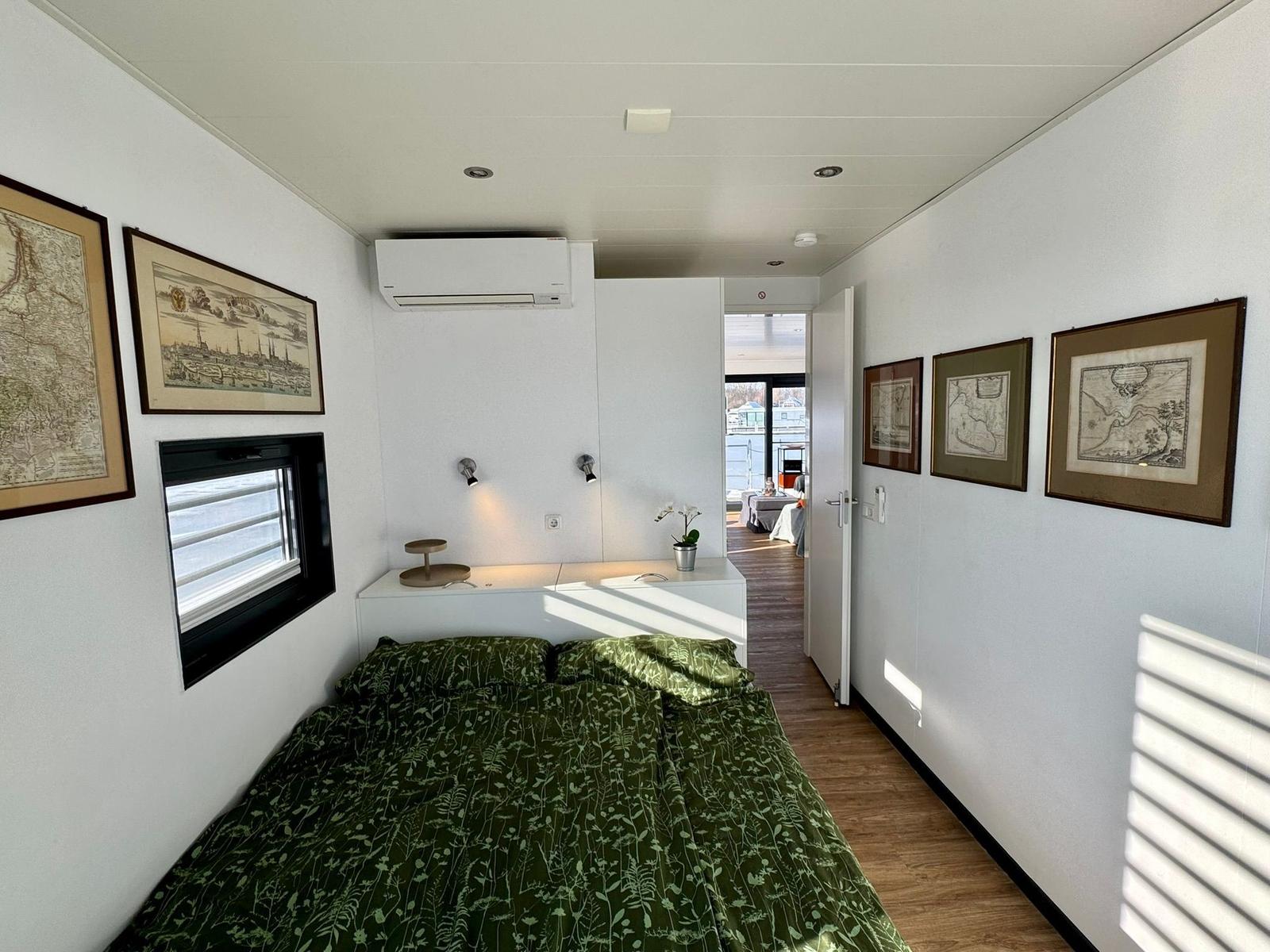 Schlafzimmer mit Bett, Wandbildern und Blick auf Terrasse.
