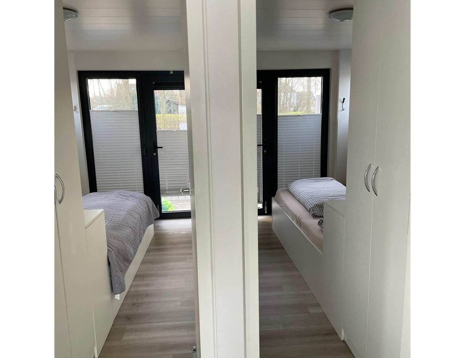 Zwei Schlafzimmer mit Betten und Schränken. Jedes Zimmer hat eine Glastür mit Jalousien.