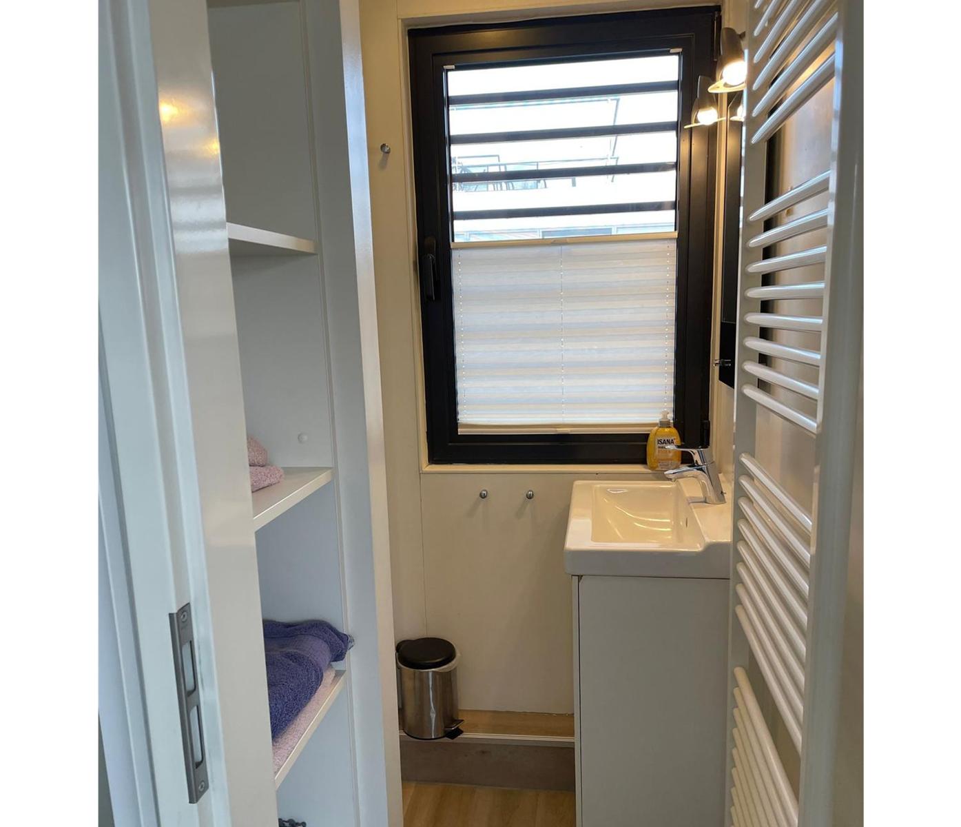 Badezimmer mit Waschbecken, Fenster und Heizung. Regal mit Handtüchern.