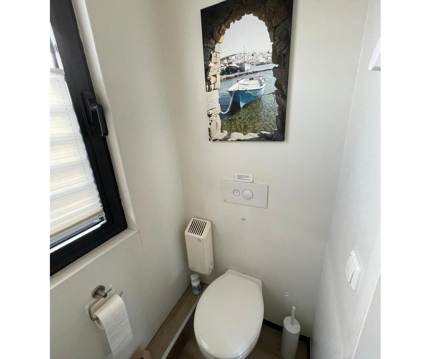 Badezimmer mit Toilette, Fenster und Wandbild eines Hafens.