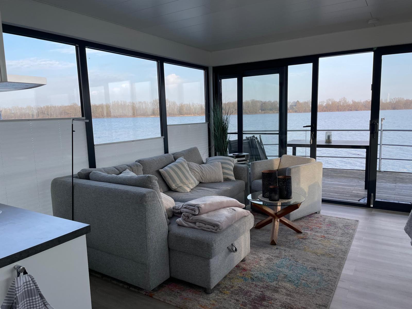 Wohnbereich mit Sofa, Sessel und Blick auf den See.