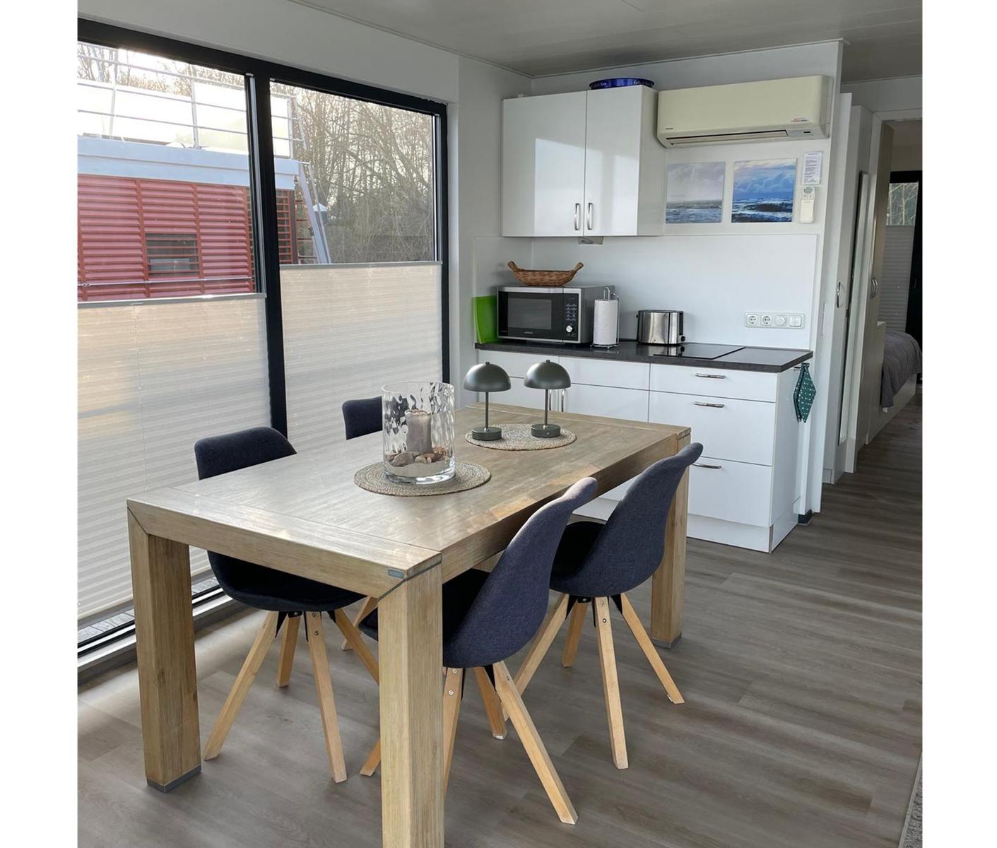 Essbereich mit Holztisch und Stühlen. Küchenzeile mit weißen Schränken und Dunstabzug.