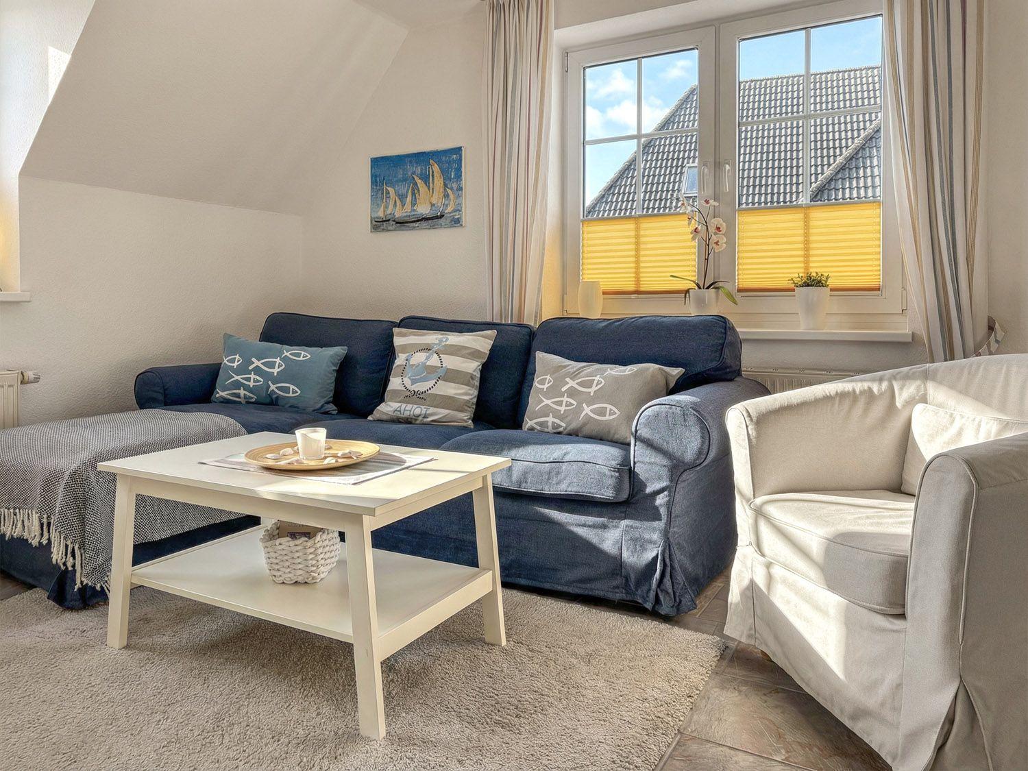 Wohnzimmer mit blauem Sofa, weißen Möbeln und Fenster mit Jalousien.