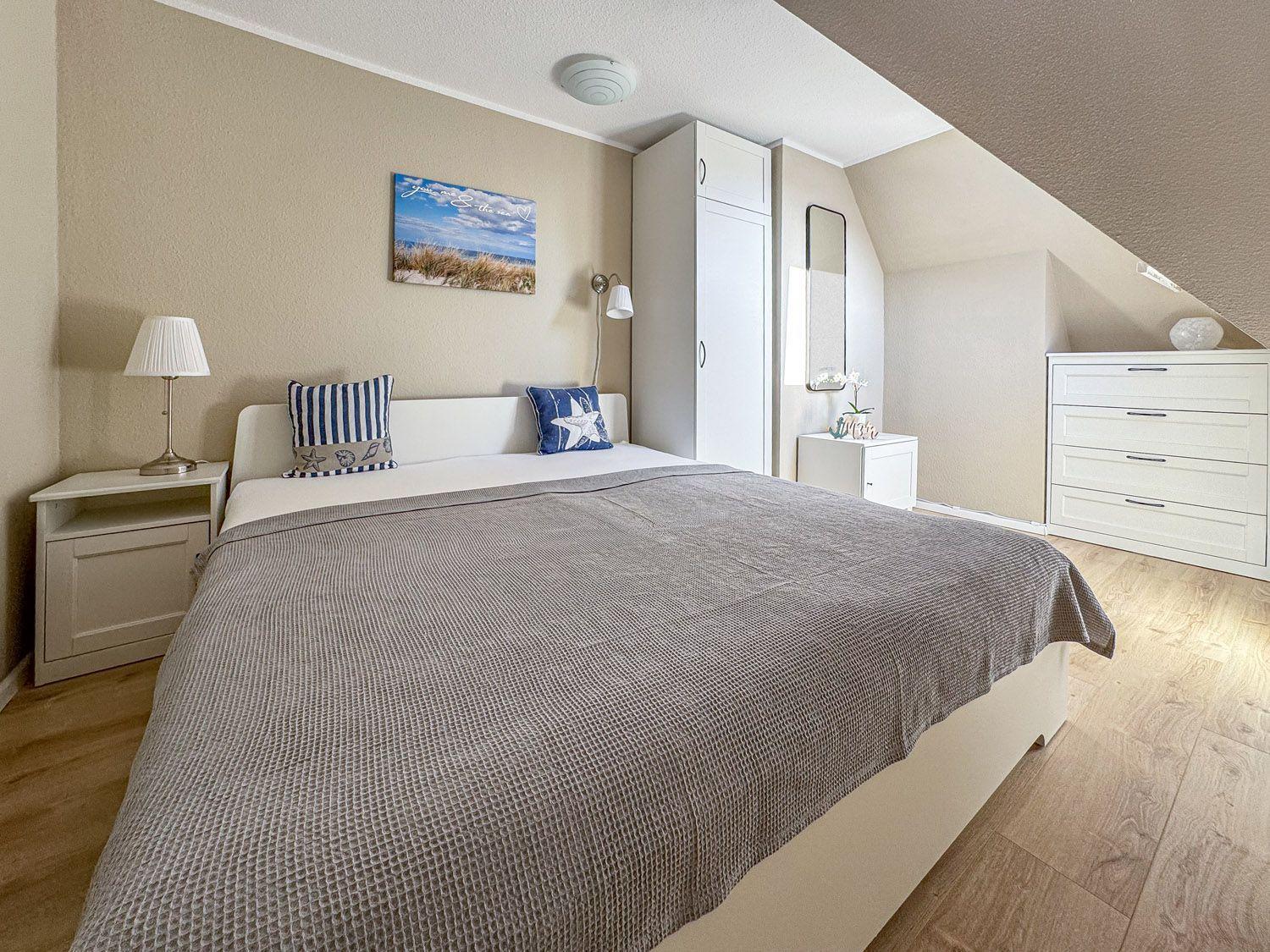 Schlafzimmer mit Doppelbett, weißen Schränken und Holzboden unter schräger Decke.