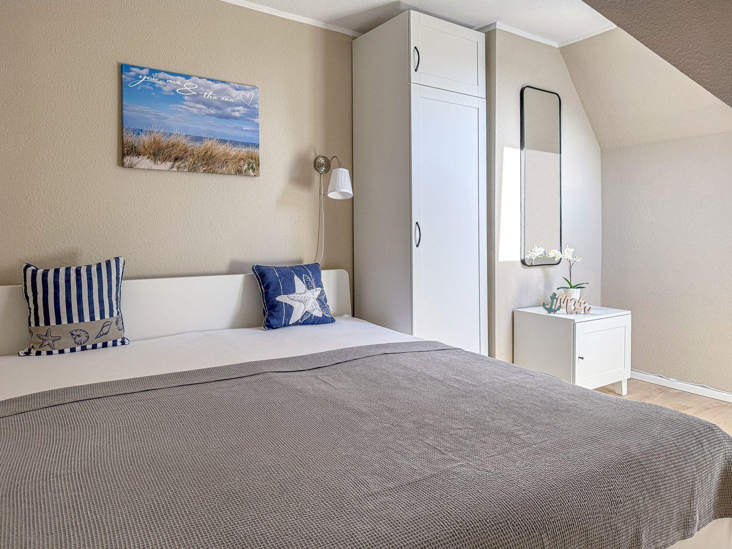 Schlafzimmer mit Bett, Kleiderschrank und Nachttisch. Wandbild und Spiegel sind sichtbar.