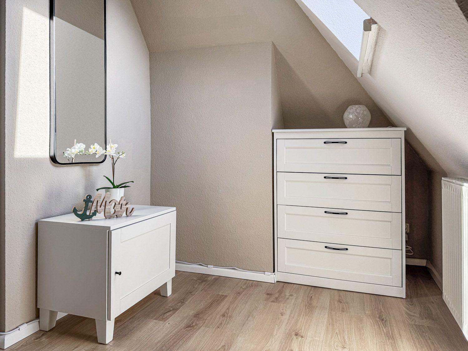 Schlafzimmer mit weißem Schrank und Spiegelschrank unter Dachschrägen.
