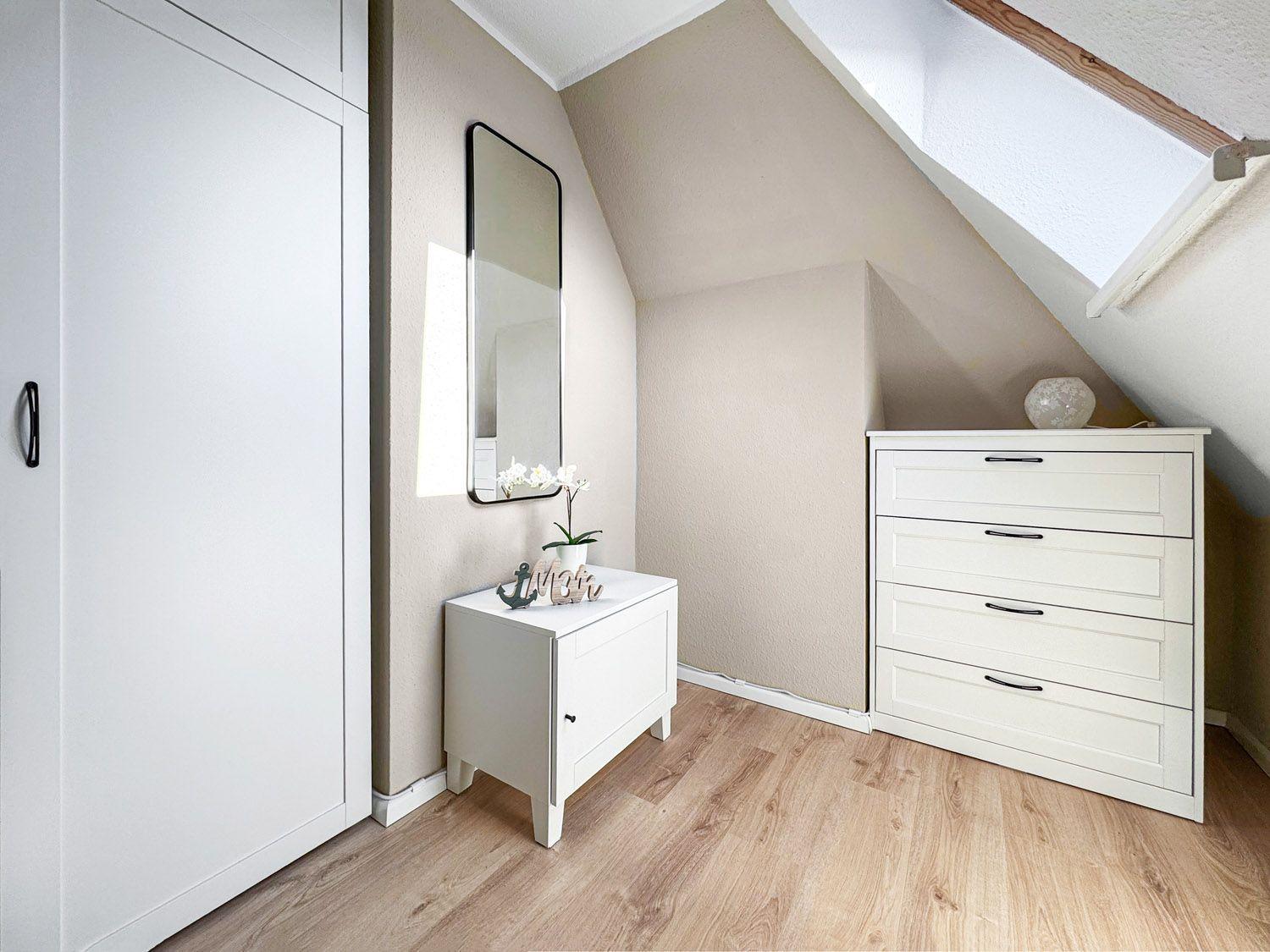 Schlafzimmer mit Dachschrägen, weißer Kommode und Spiegelschrank.