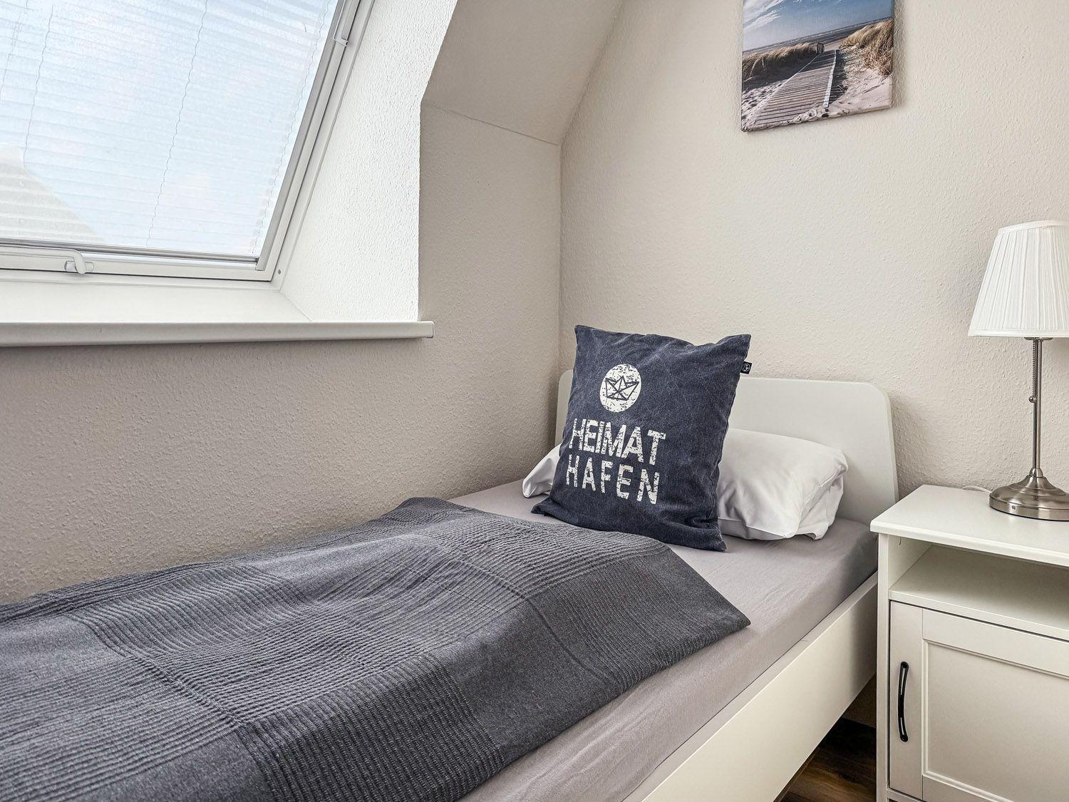 Schlafzimmer mit Dachschrägen, Fenster, Bett und Nachttisch.