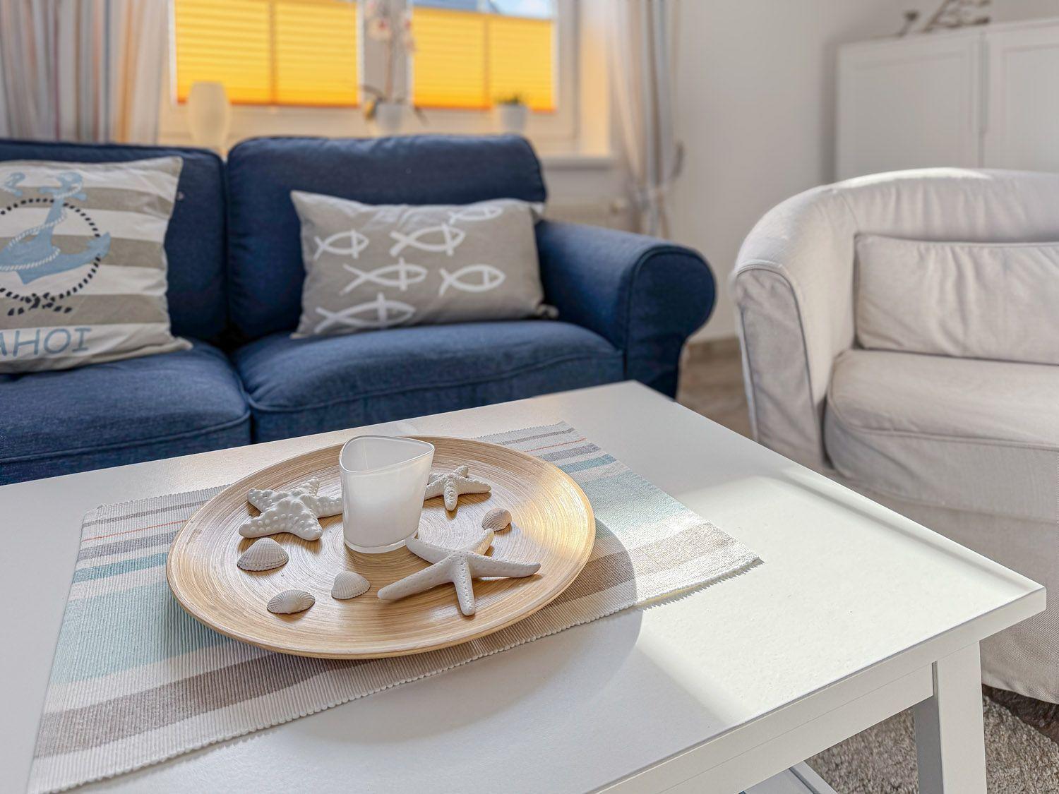 Ein Wohnzimmer mit blauem Sofa, weißem Sessel und einem Tisch mit Meeresmotiven.