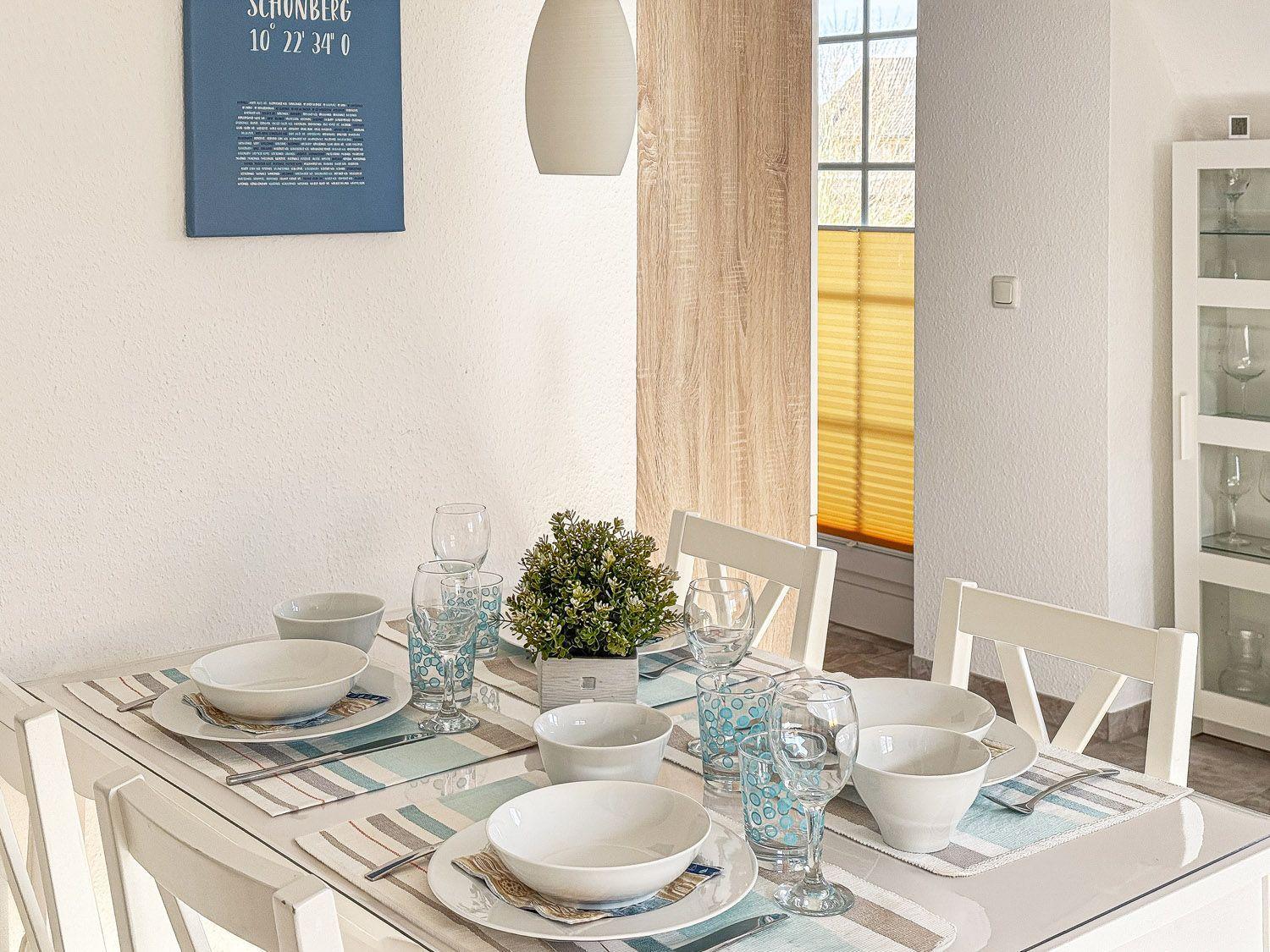 Gedeckter Esstisch mit weißen Tassen und Gläsern. An der Wand hängt ein blaues Bild.