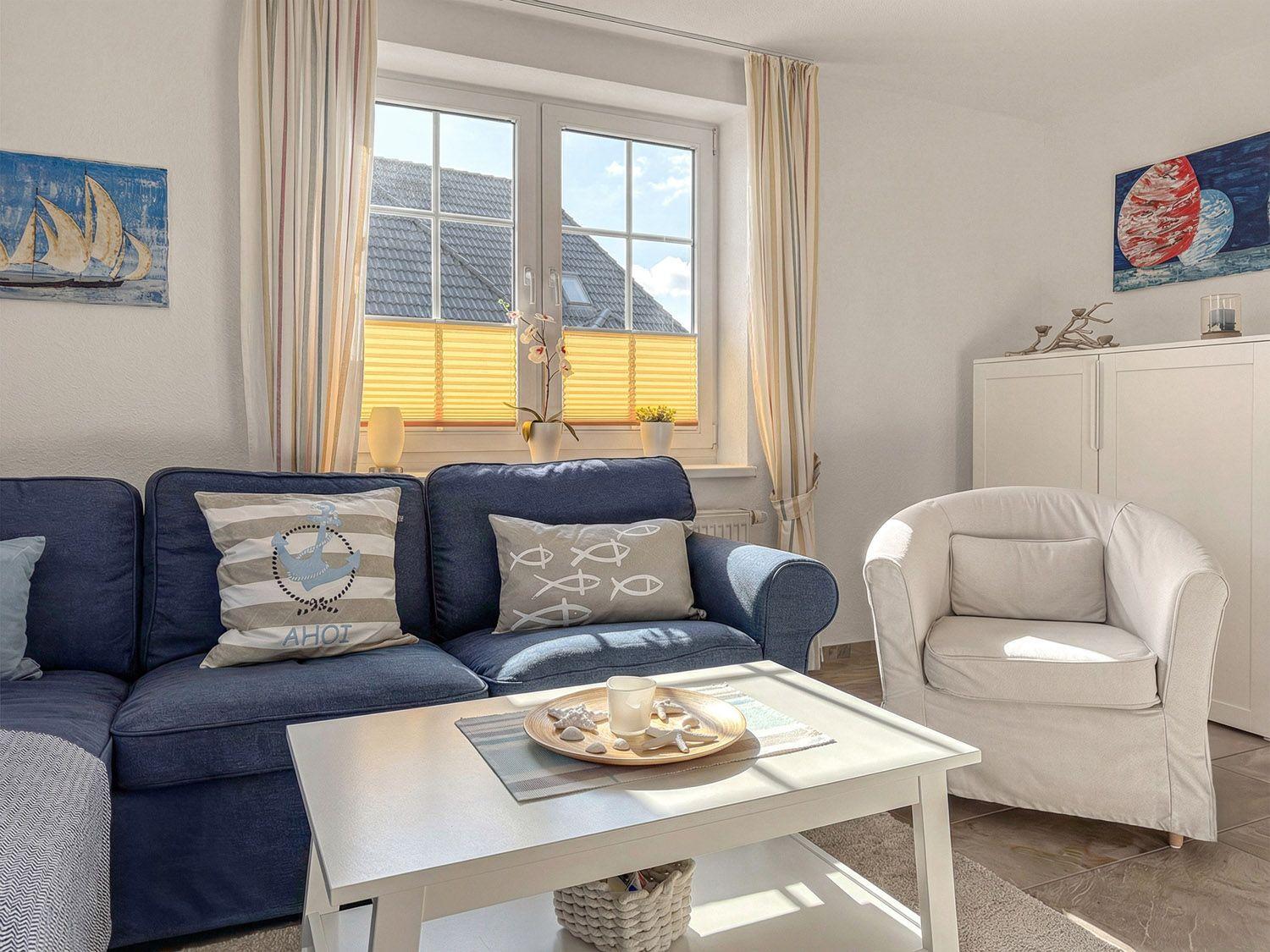 Ein Wohnzimmer mit blauem Sofa, weißem Sessel und Fenster mit Jalousien.