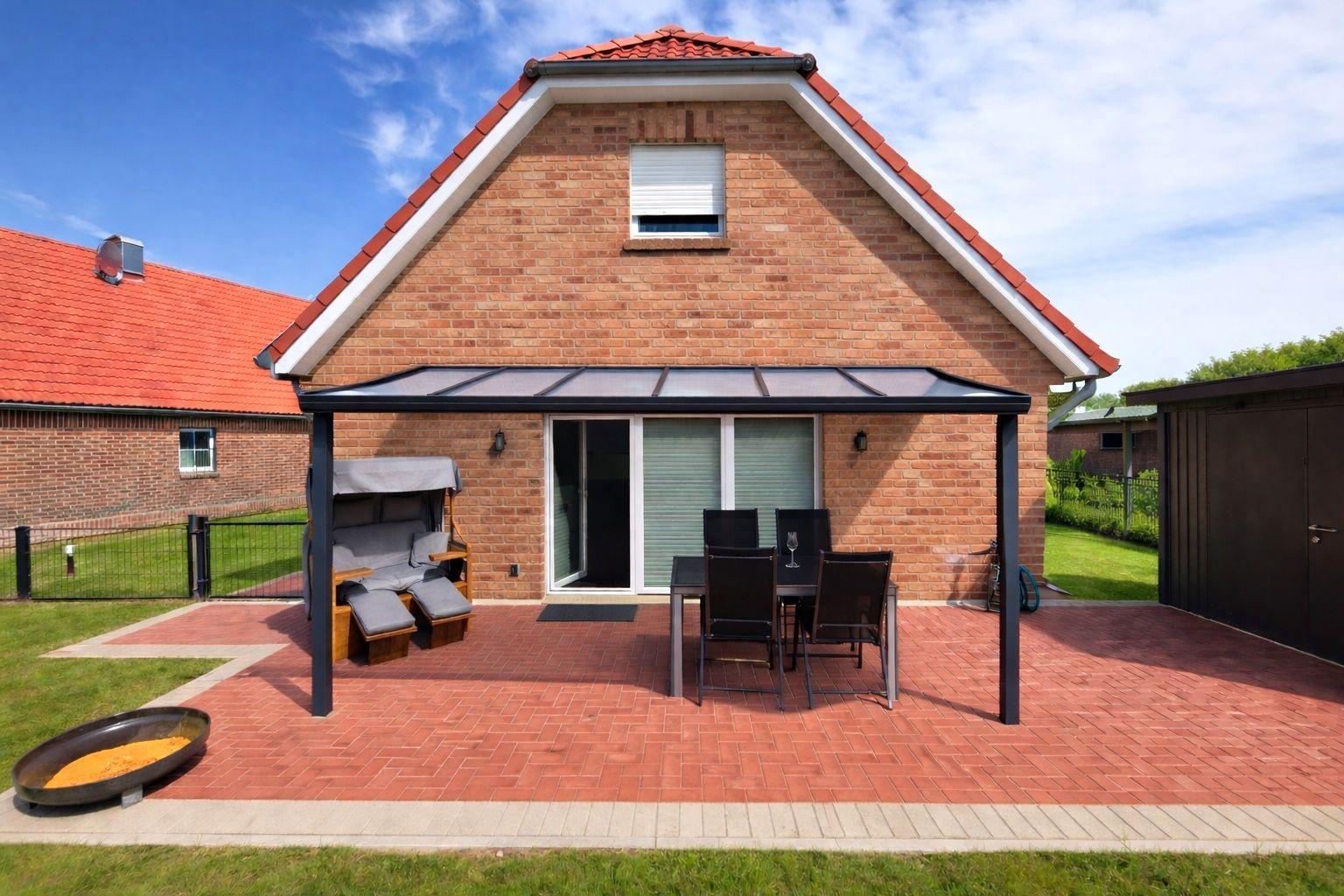 Haus mit Terrasse, Sitzgelegenheit und Grillplatz. Roter Ziegelbau mit Dachgaube.
