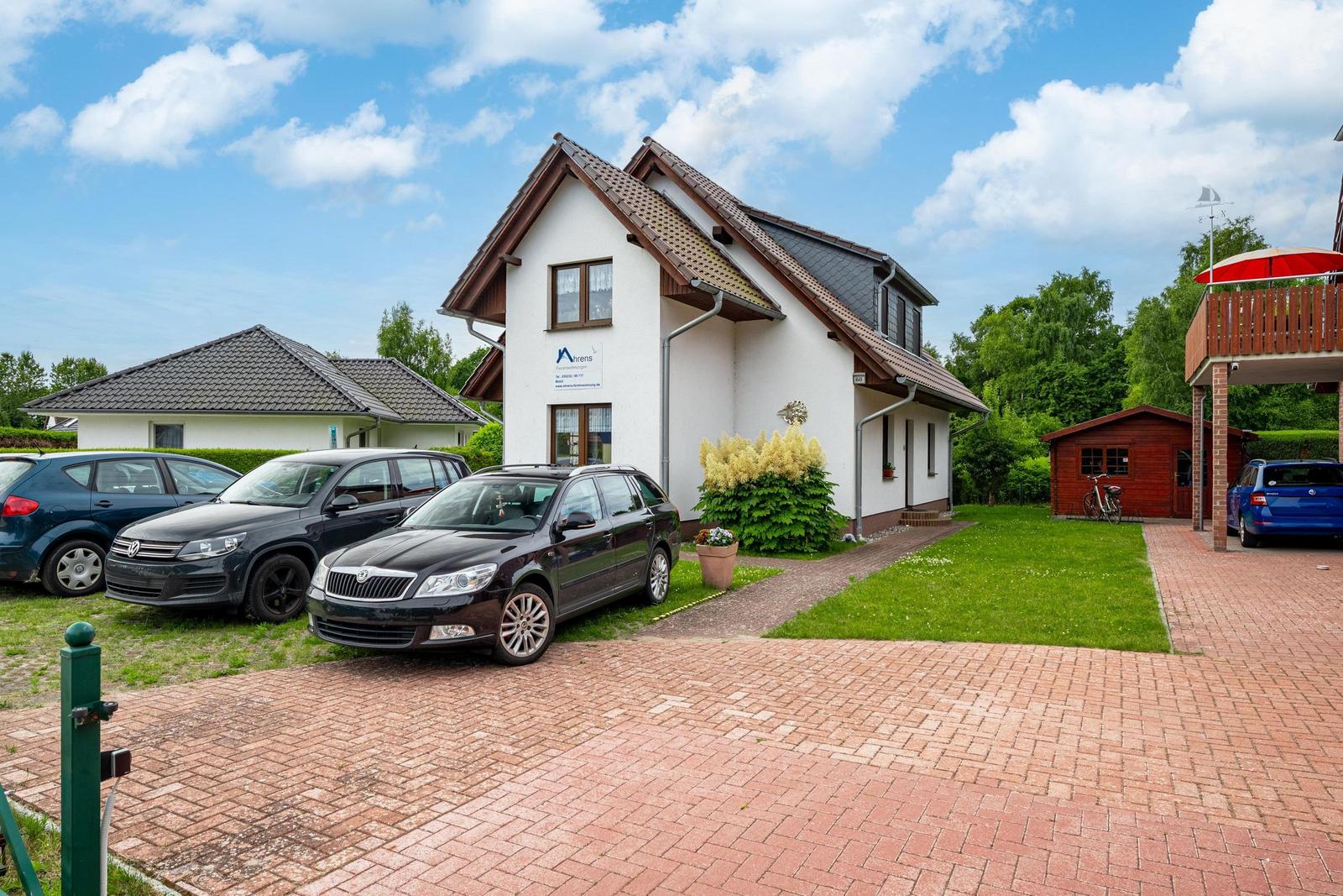 Ein zweistöckiges Haus mit Garage und Garten. Mehrere Autos stehen auf dem Hof.