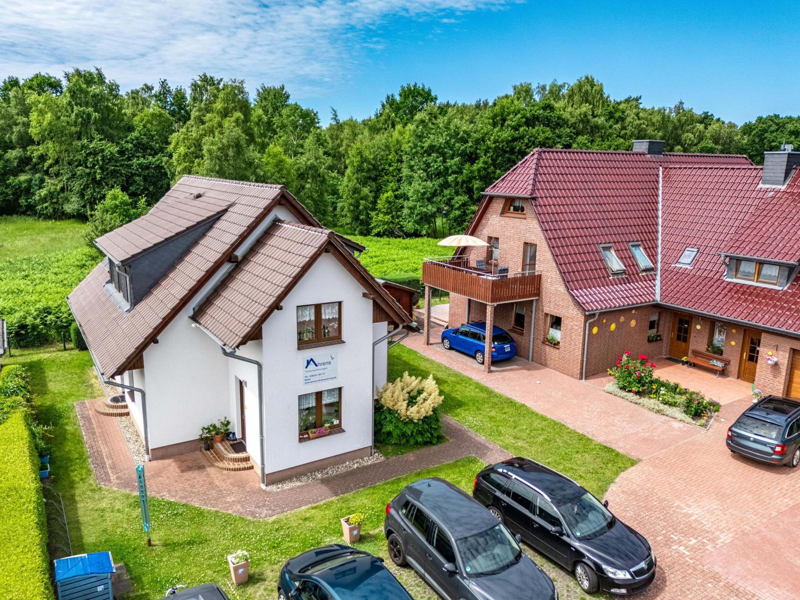 Zwei Häuser mit Garten und Parkplätzen. Ein Haus weiß, das andere rotbraun.