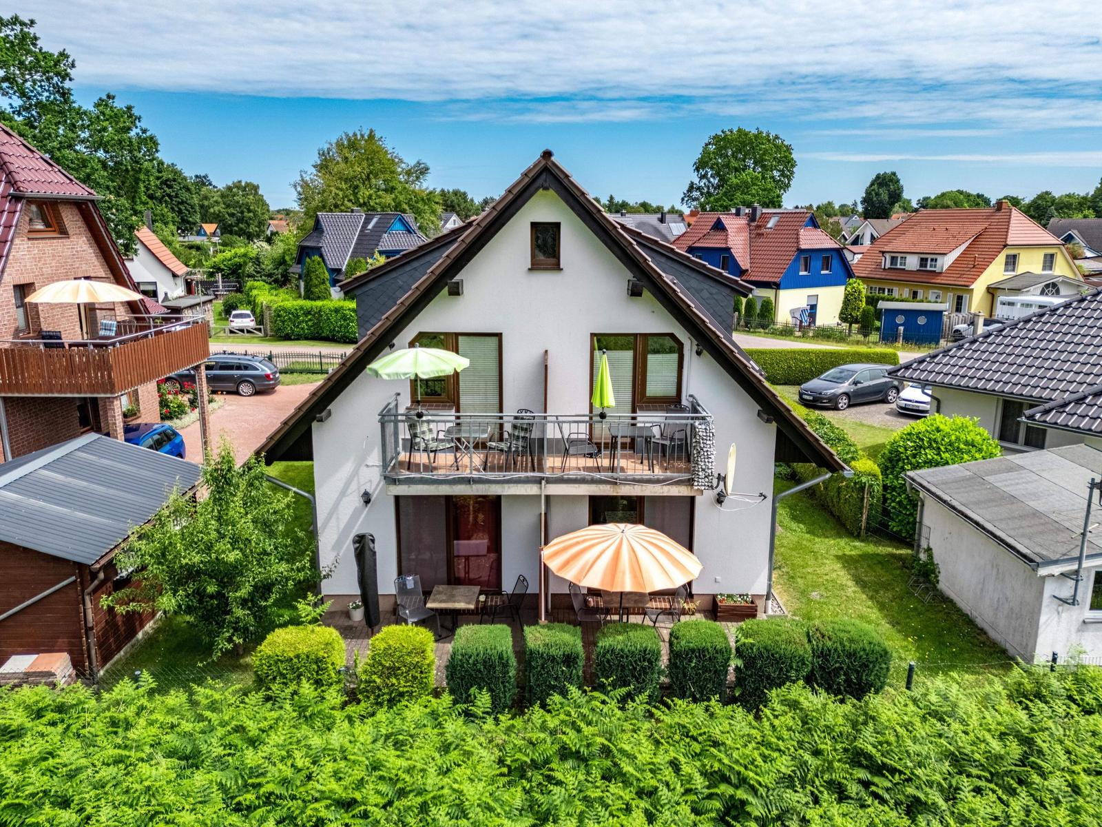 Ein zweistöckiges Haus mit Balkon und Gartenbereich mit Sonnenschirmen.