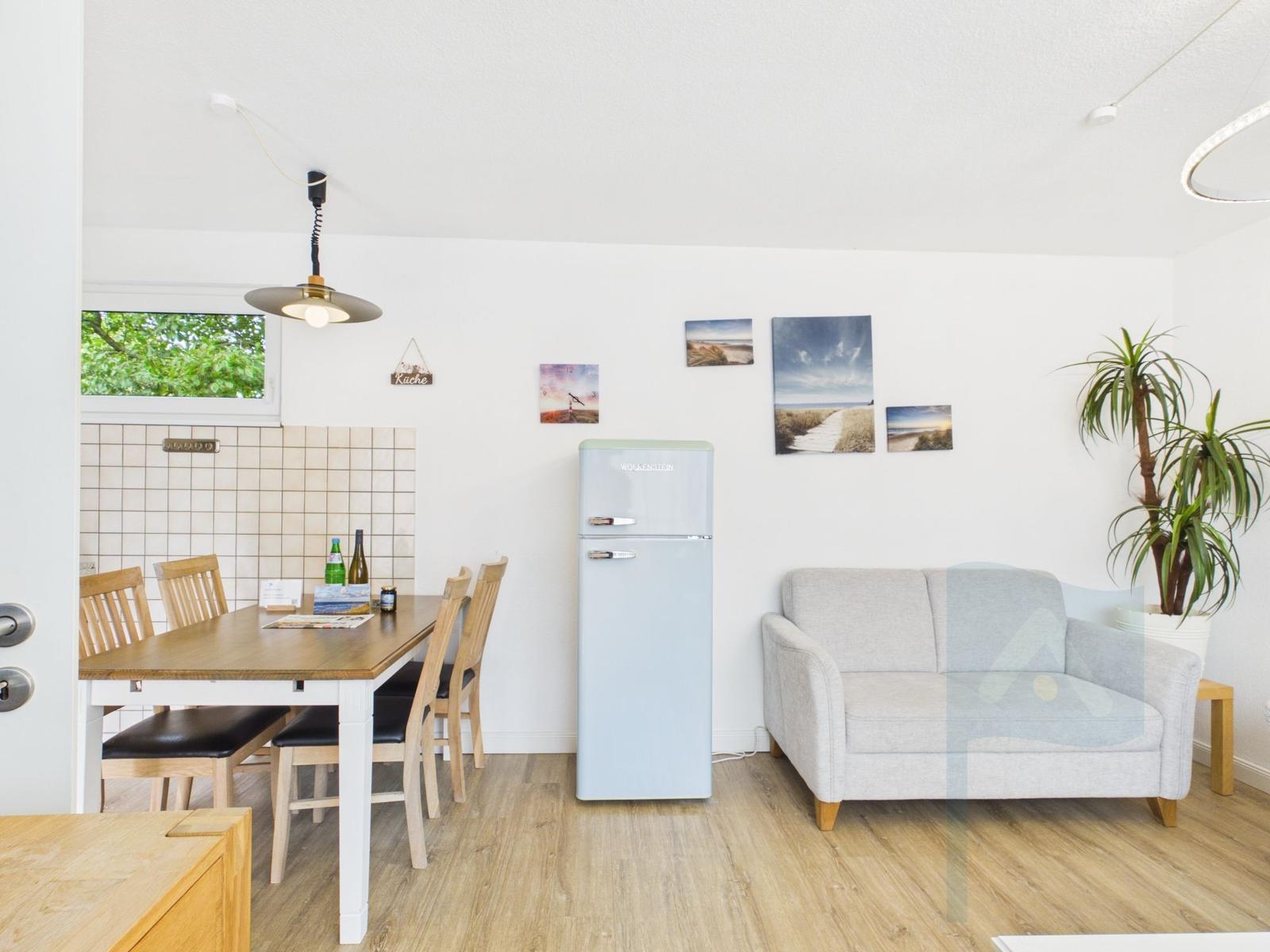 Küche mit Esstisch, Sofa und Kühlschrank. Wandbildern und Pflanze.