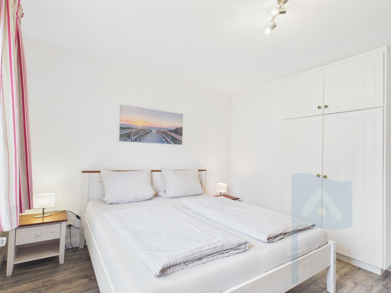 Schlafzimmer mit Doppelbett, Kleiderschrank und Nachttisch. Wandbild zeigt einen Steg.