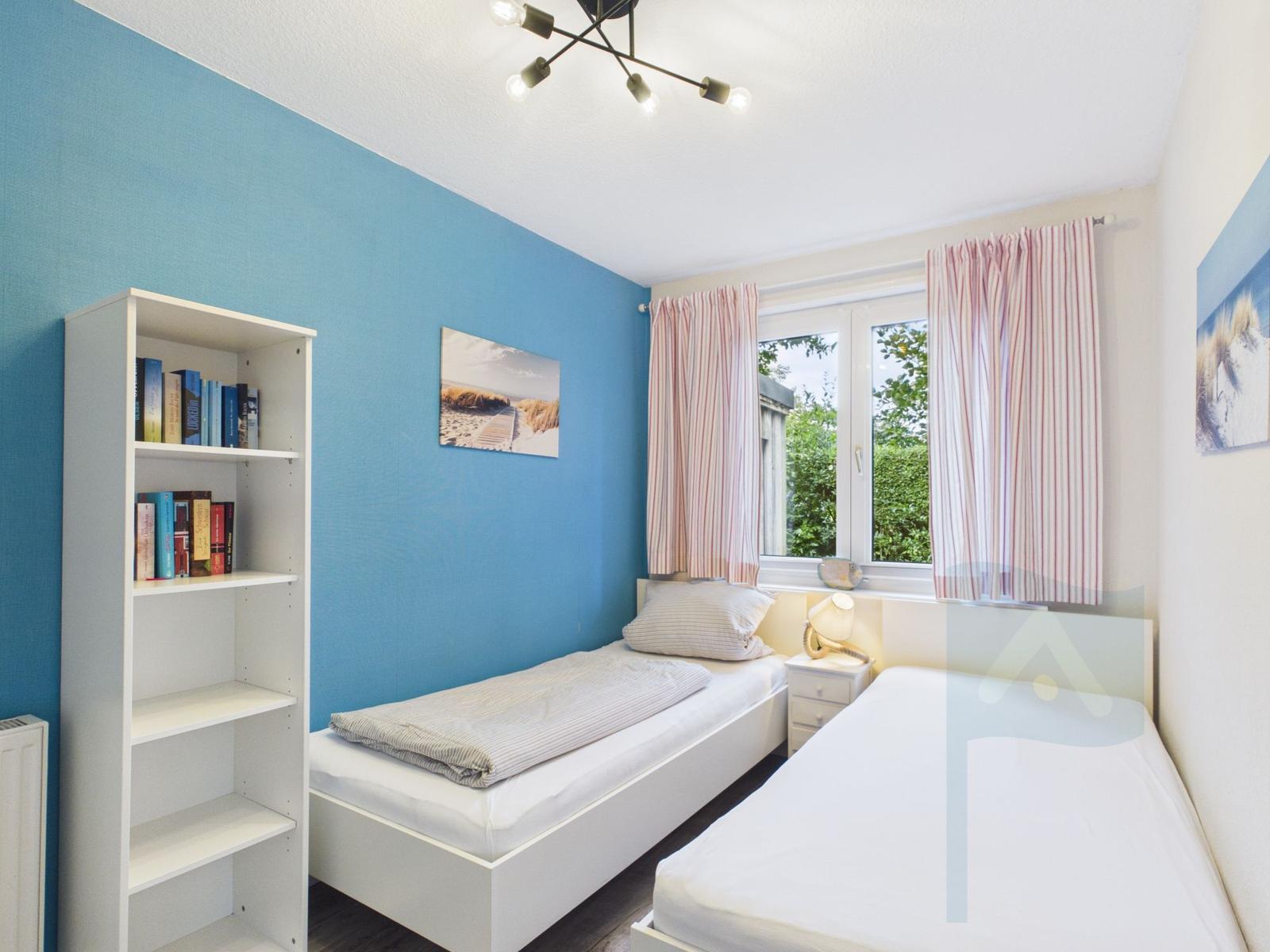 Zwei Einzelbetten, Bücherregal, Fenster mit Vorhängen, Wandbild und Deckenleuchte.