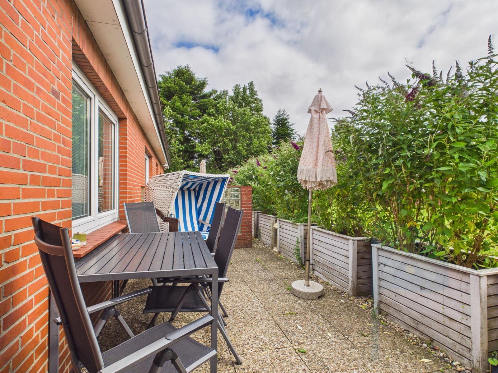Terrasse mit Tisch, Stühlen, Sonnenschirm und Liegestuhl neben rotem Backsteinhaus.